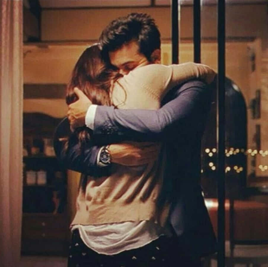 Hugging 桌布 壁紙 — 一名男子和一名女子在舒適的室內環境中溫暖地擁抱，光線柔和，背景細節模糊。