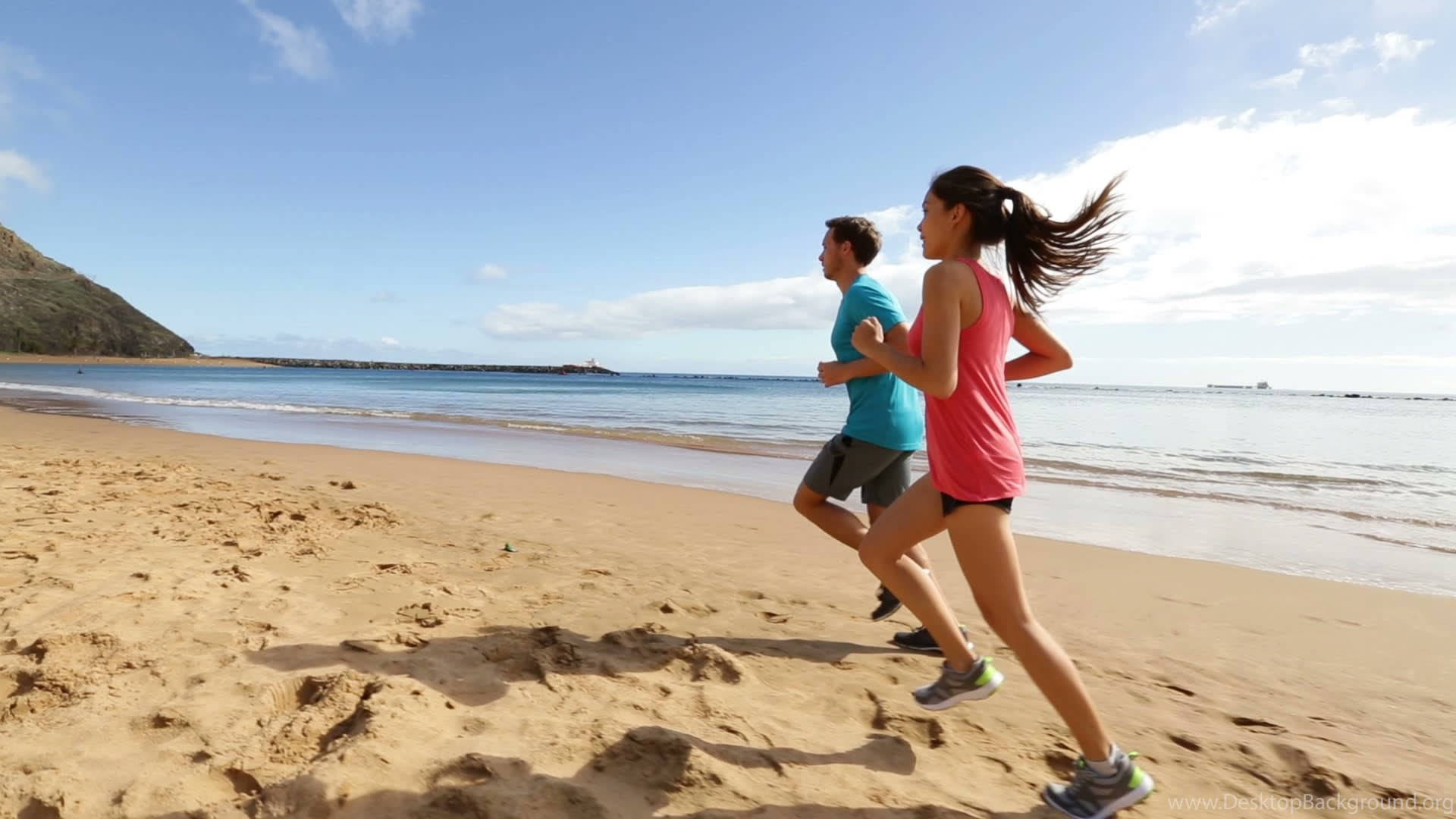 Running 桌布 壁紙 — 一名男子和一名女子沿著陽光明媚的沙灘並排慢跑，沙灘上有碧綠的海浪和清澈的藍天。