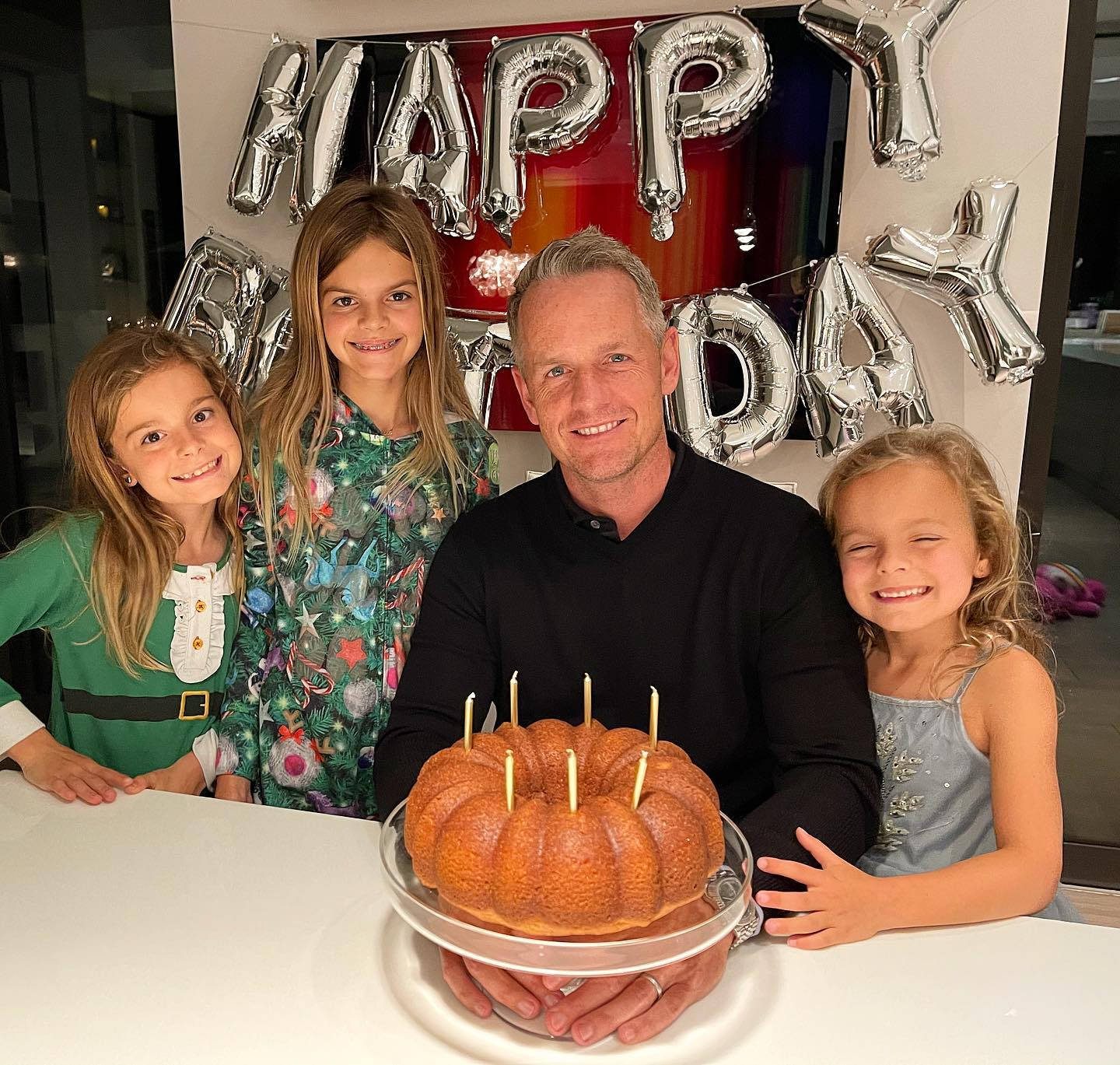 Family 桌布 壁紙 — 一名男子和三個微笑的女孩在銀色「HAPPY BIRTHDAY」氣球下圍著一個插有蠟燭的環形蛋糕擺姿勢。
