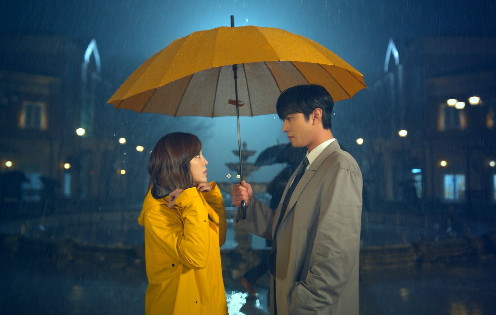 Proposal 桌布 壁紙 — 一名男子和女子在夜晚雨中的城市燈光下共享一把亮黃色的雨傘。