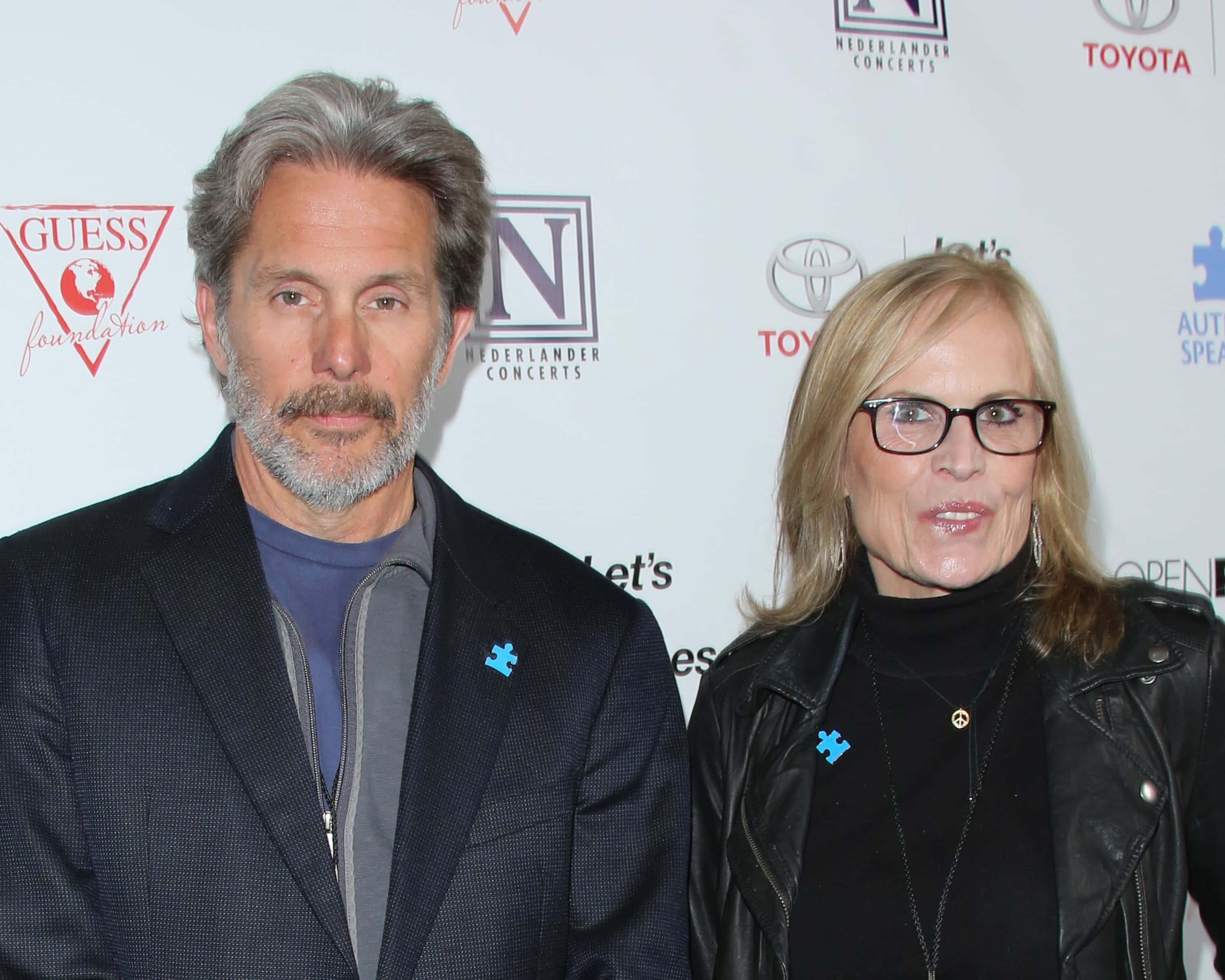 Gary Cole 桌布 壁紙 — 一名男子和女子在慈善活動中並肩站立，佩戴藍色拼圖別針，背景為品牌背景。