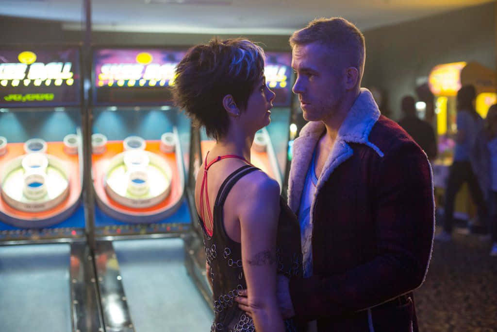 Deadpool And Vanessa 桌布 壁紙 — 一名男子和女子在昏暗的遊戲機中心內緊靠站立，被身後發光的遊戲機照亮。