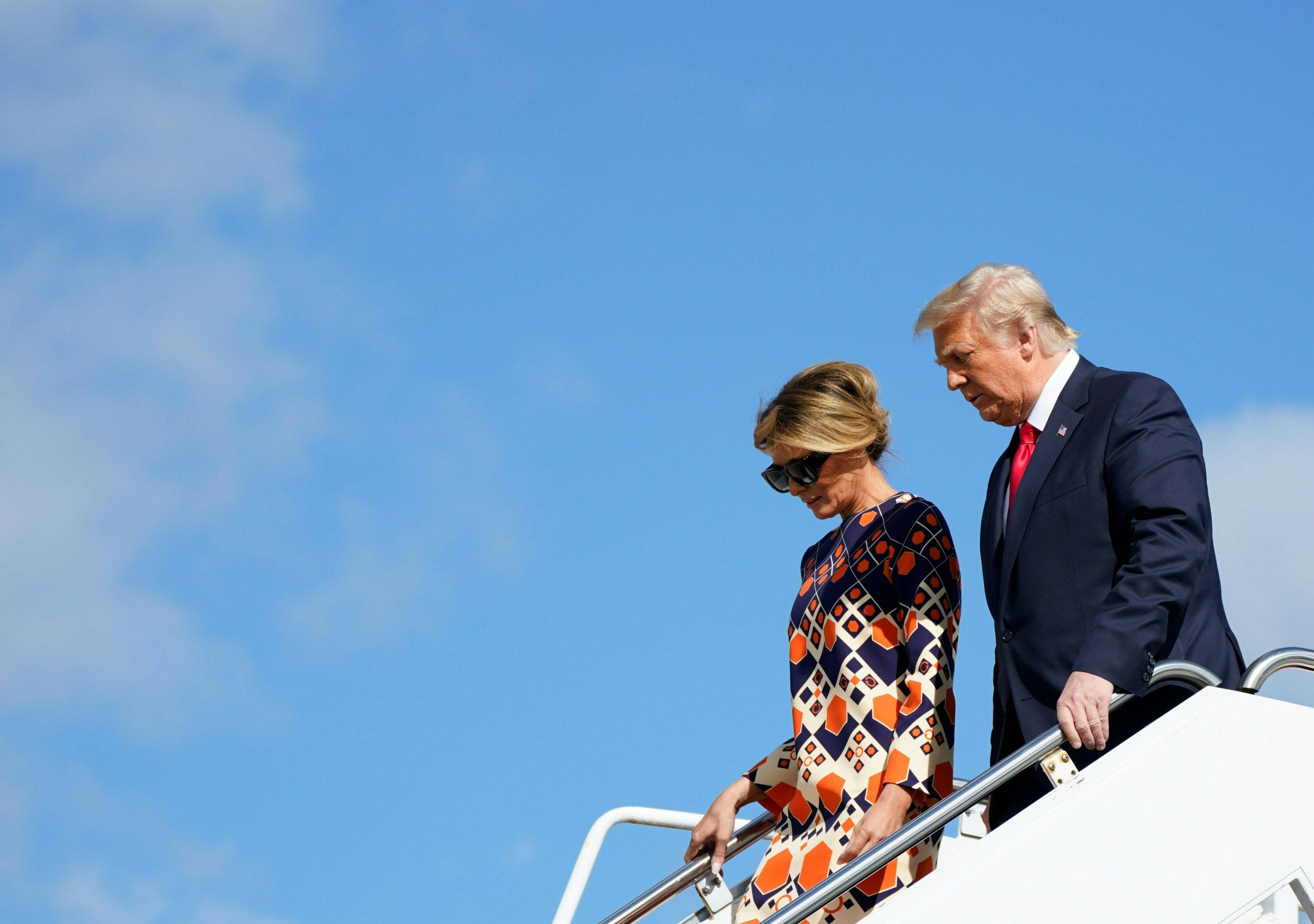 Melania 桌布 壁紙 — 一名男子和女子在晴朗藍天白雲下走下飛機樓梯。