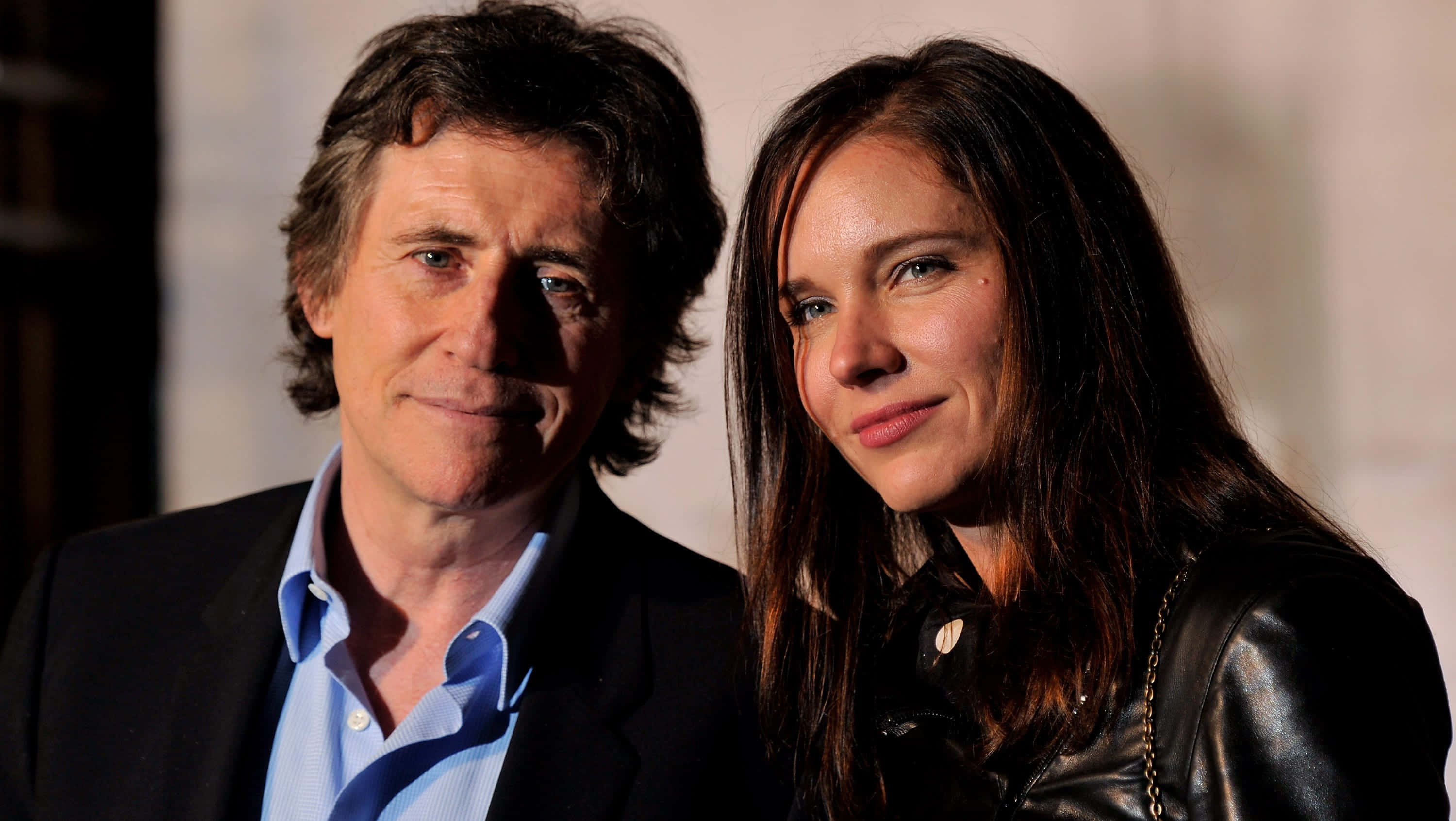Gabriel Byrne 桌布 壁紙 — 一名男子和女子在柔和燈光下緊密站在一起，兩人都帶著溫柔的微笑看向相機。