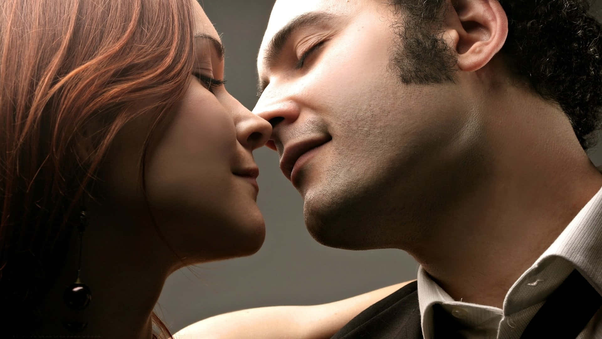 couple love 桌布 壁紙 — 一名男子和女子閉上眼睛，在柔和的灰色背景前傾身親吻。