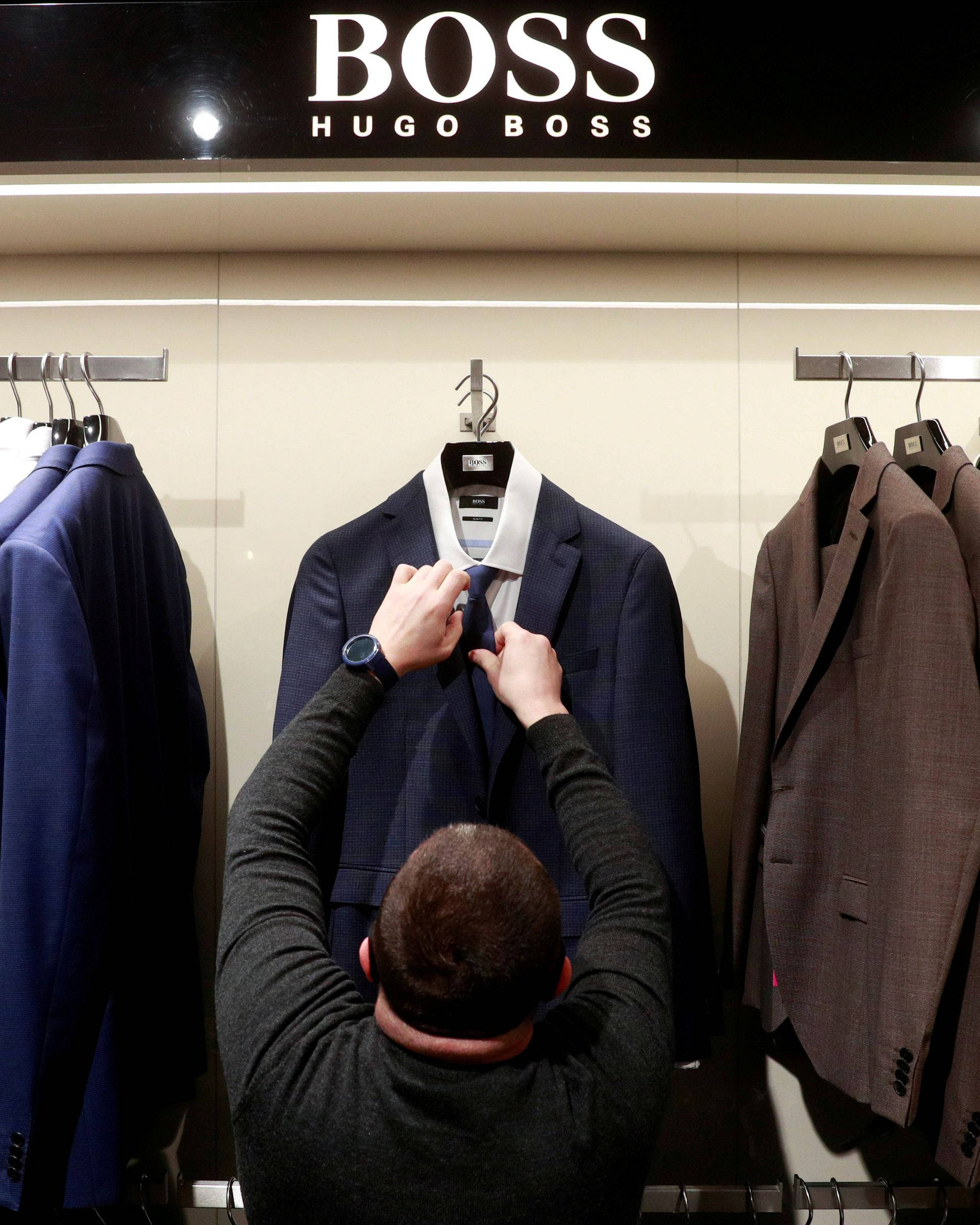 Clothes 桌布 壁紙 — 一名男子在 Hugo Boss 精品店明亮的店舖燈光下調整人體模型上的海軍藍西裝領帶。