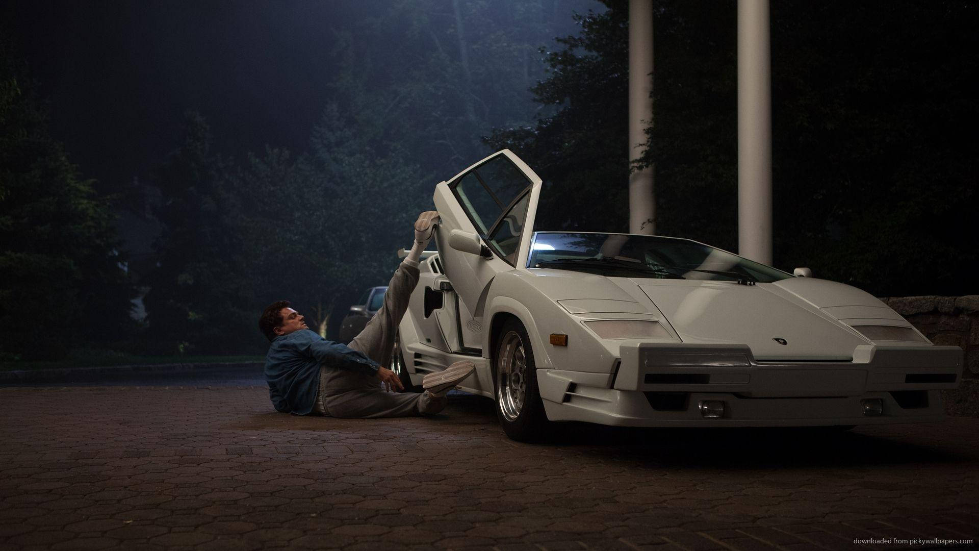 Wolf Of Wall Street 桌布 壁紙 — 一名男子在夜晚靠在一輛白色藍寶堅尼Countach旁邊，其剪刀門在戲劇性燈光下打開。