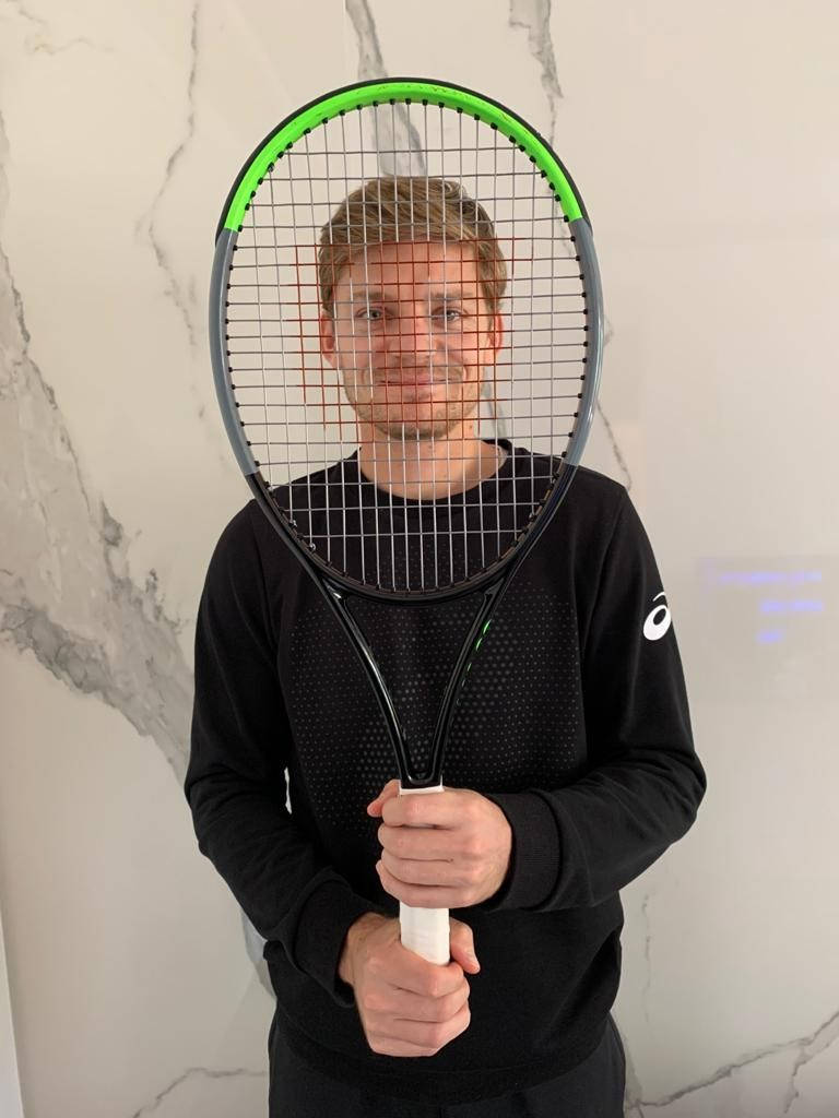 Tennis 桌布 壁紙 — 一名男子在大理石牆前將網球拍舉在臉前，對著鏡頭微笑。
