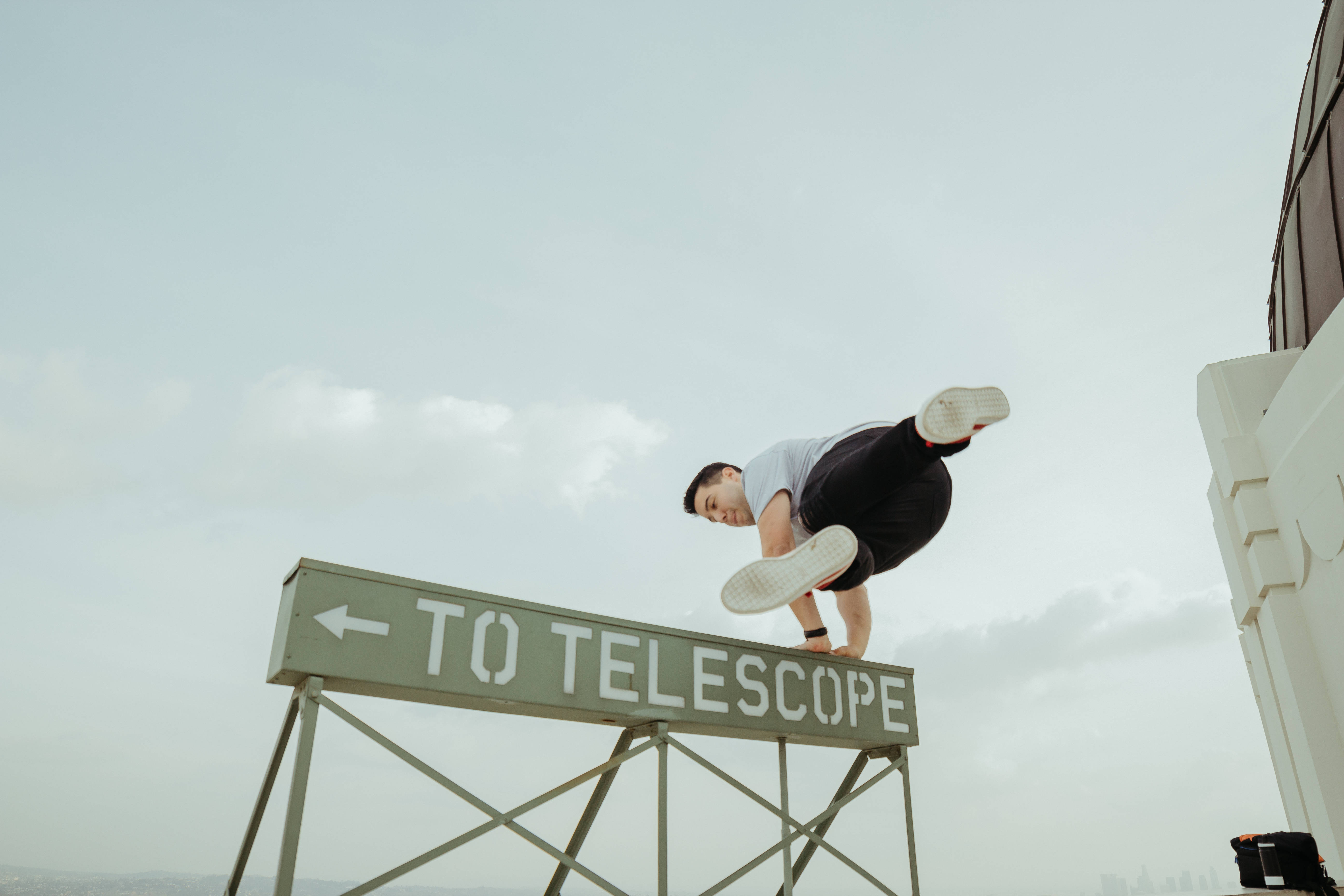 Parkour 桌布 壁紙 — 一名男子在寫有「TO TELESCOPE」的標誌上做倒立，背景是多雲的天空。