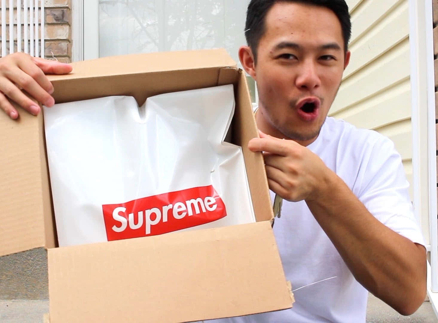 supreme 桌布 壁紙 — 一名男子在屋外興奮地從紙箱中揭開一件Supreme品牌襯衫。