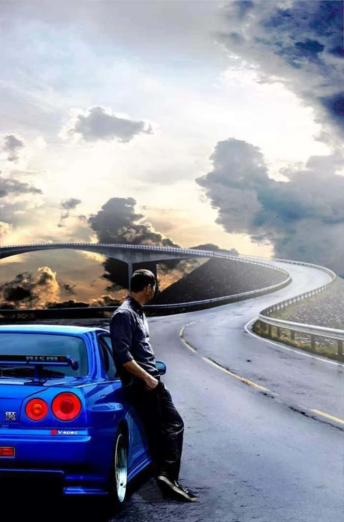 Paul Walker Skyline 桌布 壁紙 — 一名男子在戲劇性的多雲天空下，靠在一輛藍色跑車上，位於蜿蜒的山路上。