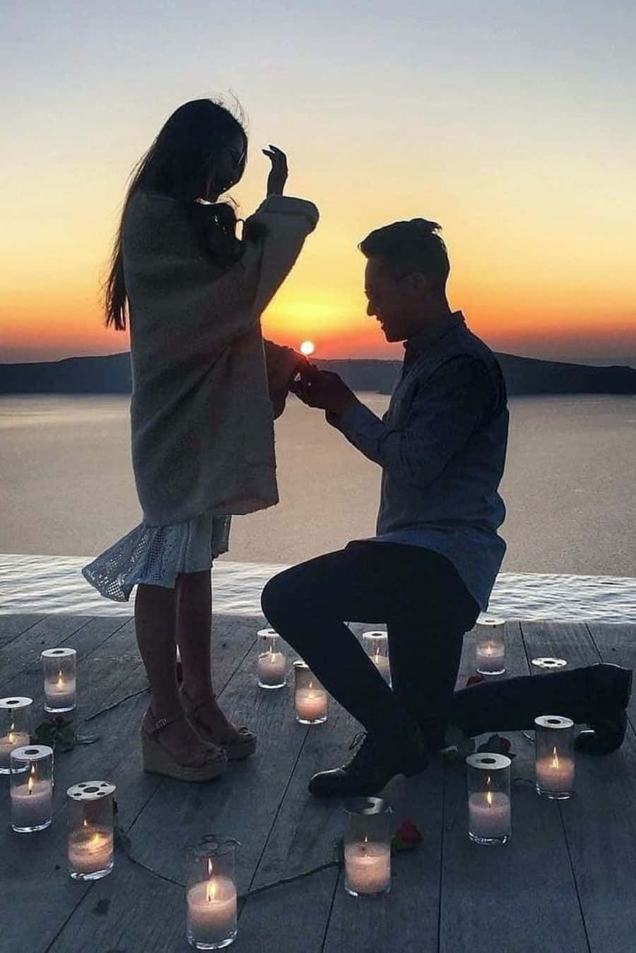 Proposal 桌布 壁紙 — 一名男子在日落時分跪在木碼頭的燭光旁，向一位因喜悅而掩面的女子求婚。