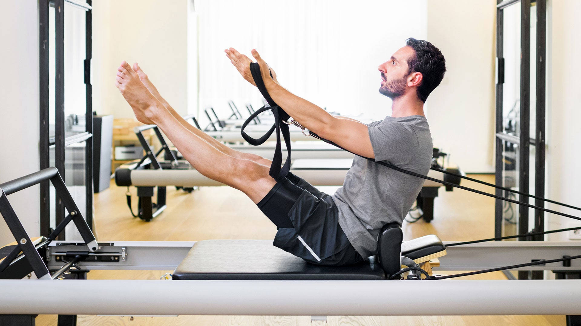 Exercise 桌布 壁紙 — 一名男子在明亮現代的工作室中，於木地板和鏡面牆的環境下，在塑身機上進行皮拉提斯運動。