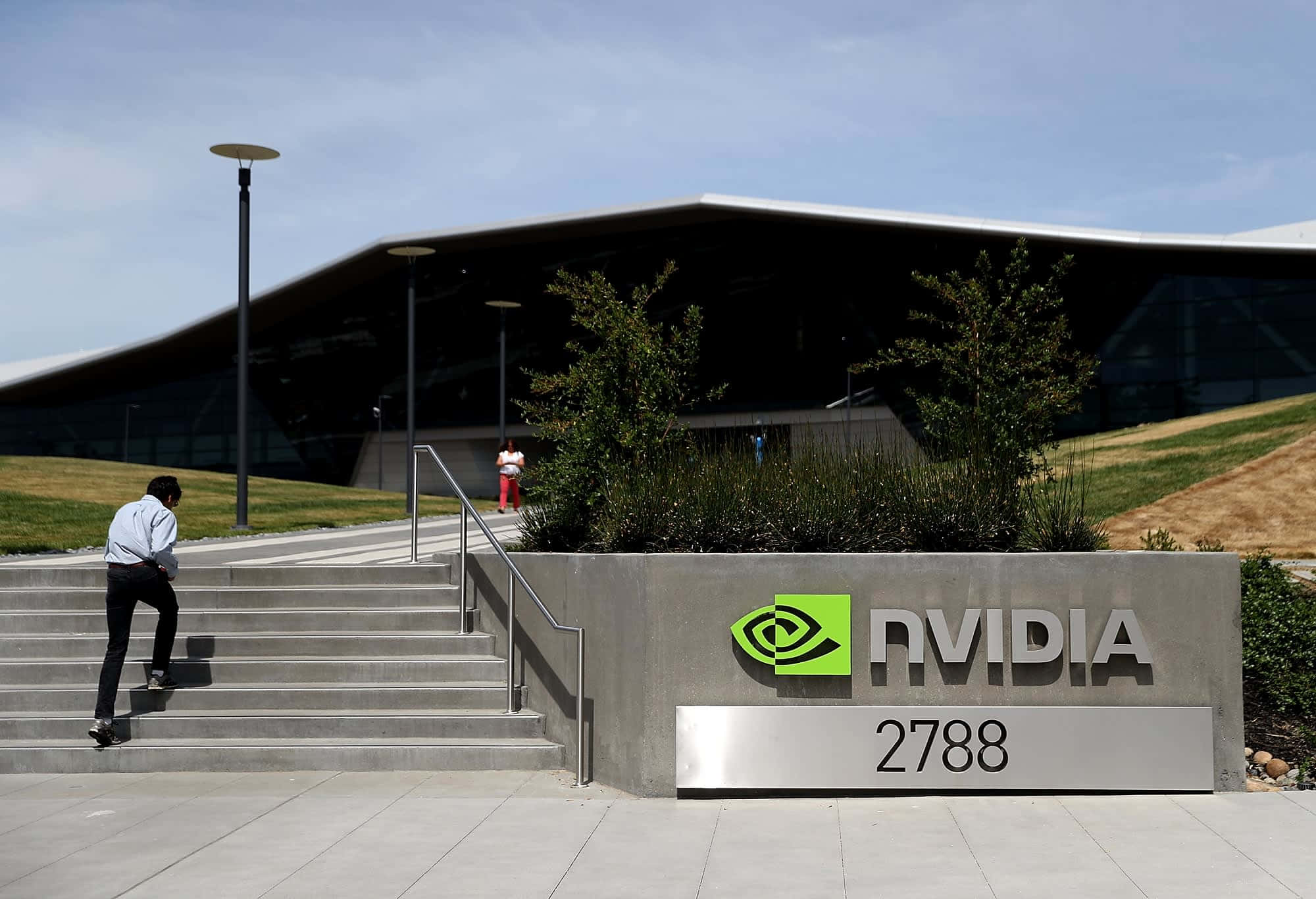 nvidia 桌布 壁紙 — 一名男子在晴朗的藍天下走上混凝土階梯，前往現代化的NVIDIA企業大樓。