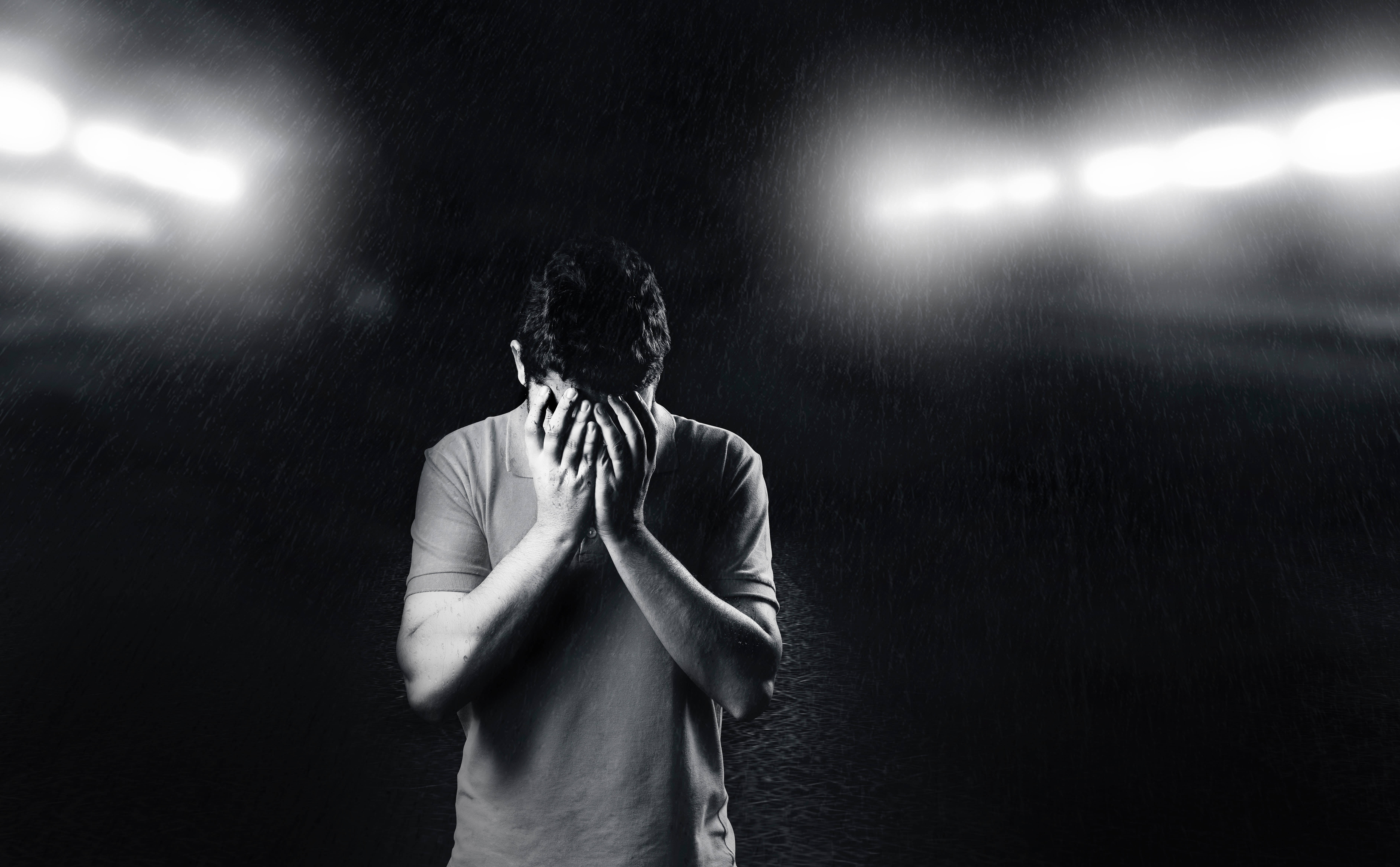 Monochrome 桌布 壁紙 — 一名男子在暴雨中，於球場燈光下絕望地掩面，黑白照片。