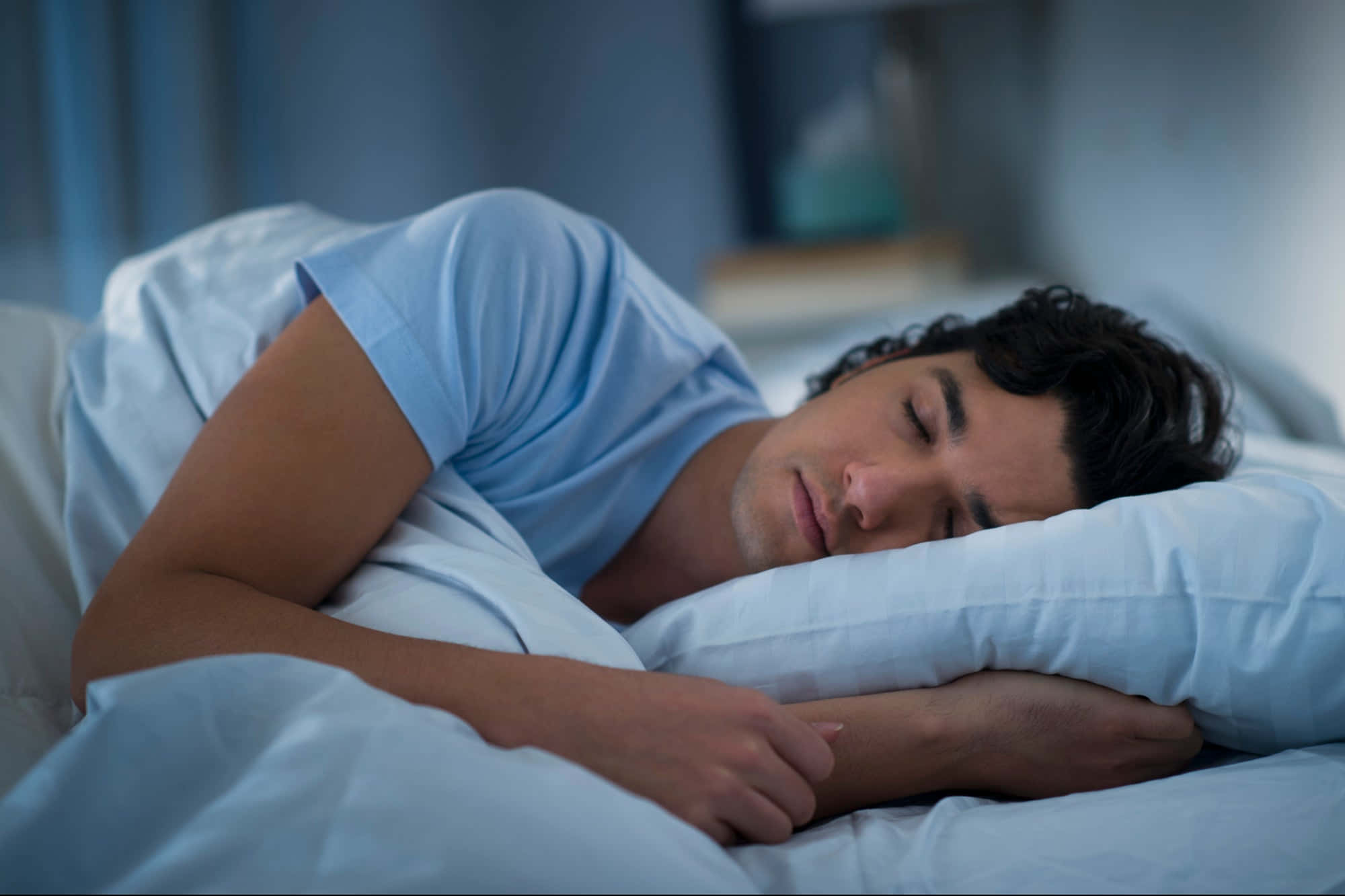 Sleep 桌布 壁紙 — 一名男子在柔和燈光、藍色調和白色床品的臥室中側臥安睡。
