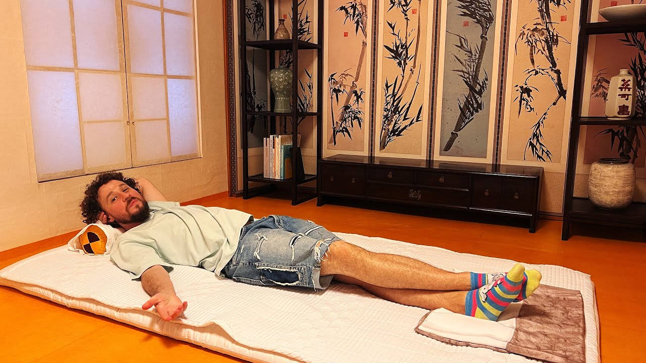 日本 桌布 壁紙 — 一名男子在溫暖燈光的日式房間內，在榻榻米上放鬆休息，房間有竹屏風和木架。