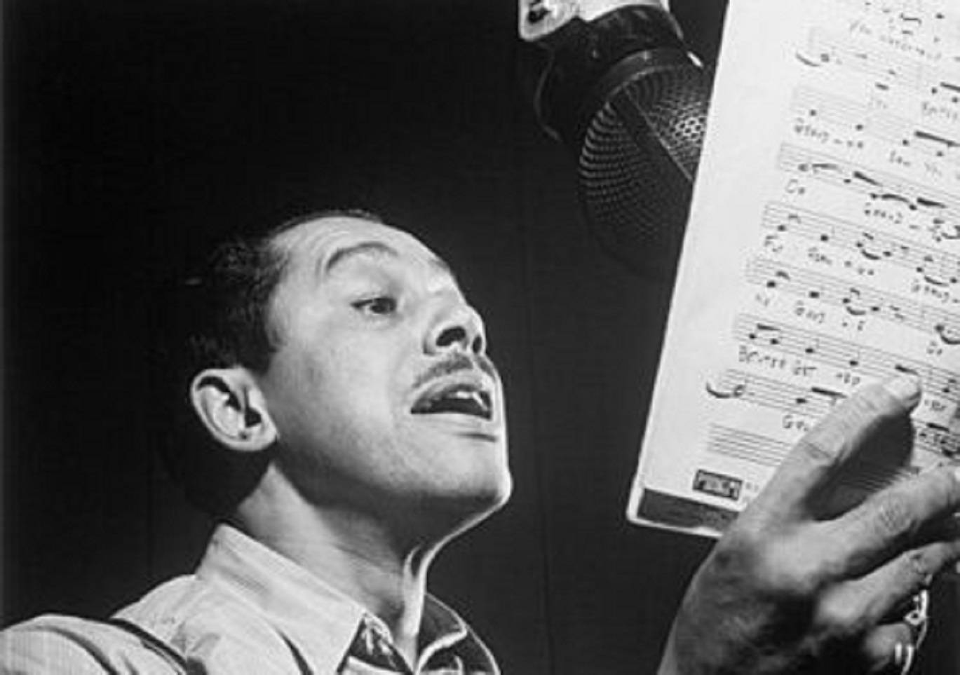 Singing 桌布 壁紙 — 一名男子在燈光昏暗的錄音室中，手持樂譜，對著復古麥克風深情演唱。