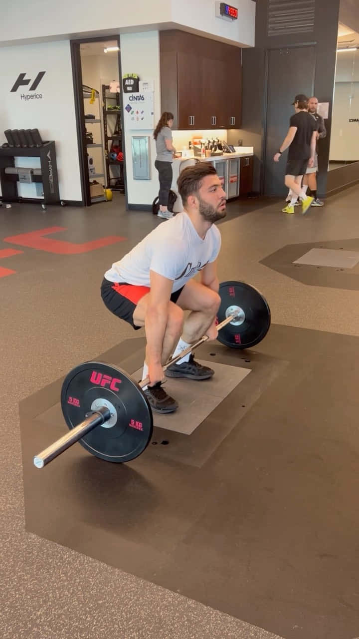 Fitness 桌布 壁紙 — 一名男子在現代健身房用槓鈴進行深蹲，背景有其他人在鍛煉。