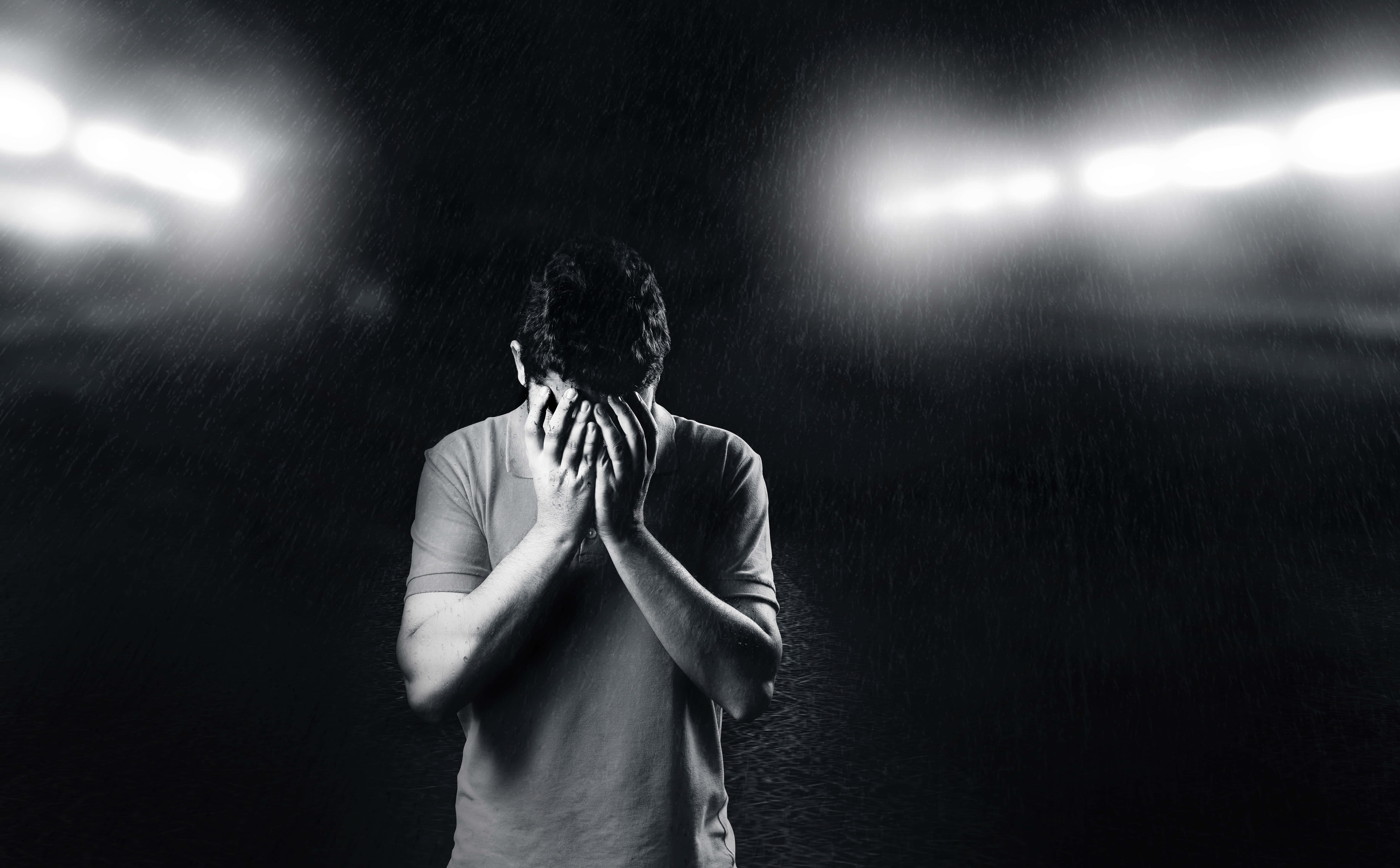 Man Standing 桌布 壁紙 — 一名男子在球場燈光下，於傾盆大雨中絕望地掩面，黑白照片。