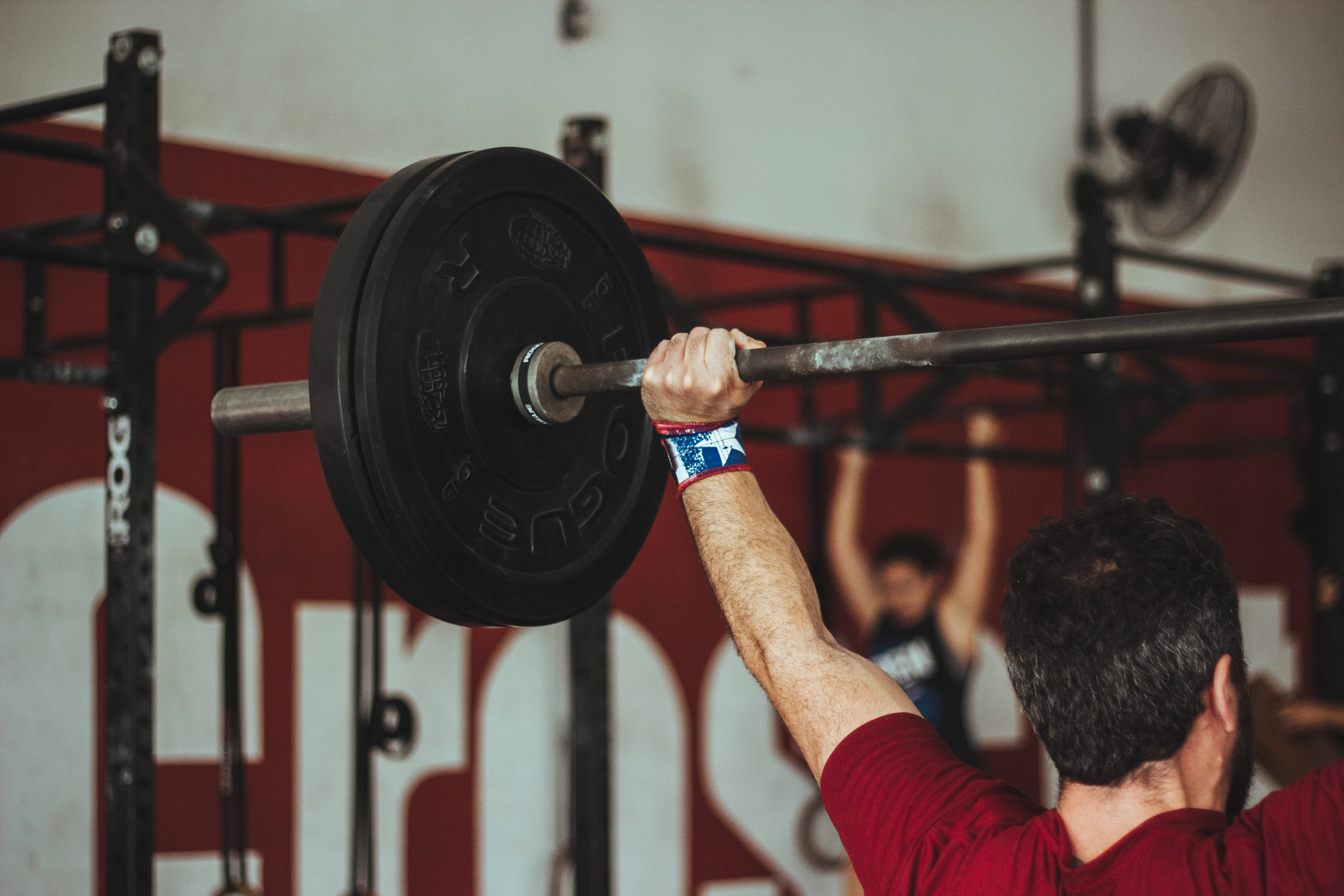 Barbell 桌布 壁紙 — 一名男子在紅色牆壁和可見設備的健身房中舉起沉重的槓鈴。