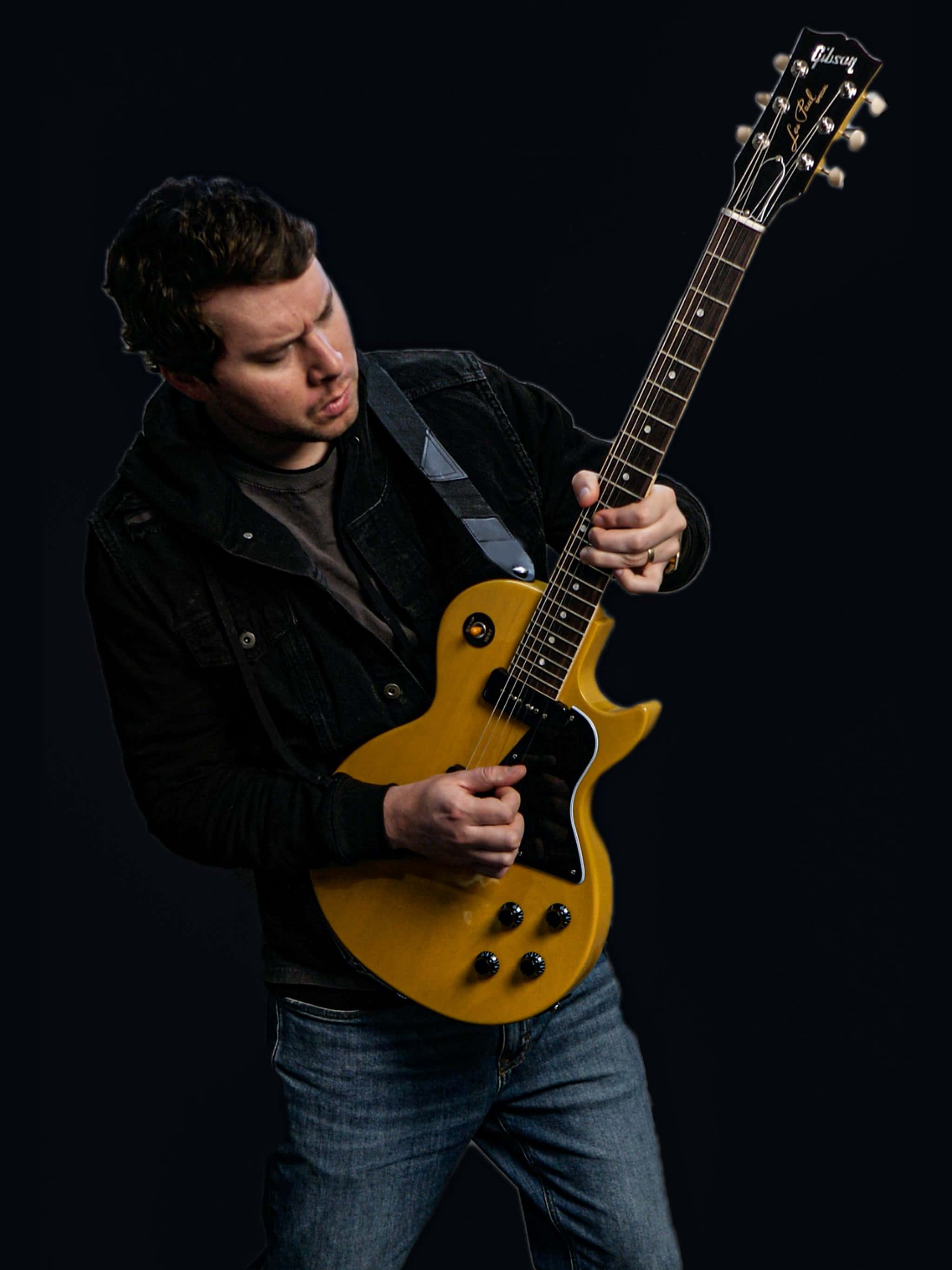 音樂 桌布 壁紙 — 一名男子在純黑背景下激烈地彈奏黃色Gibson Les Paul電吉他。