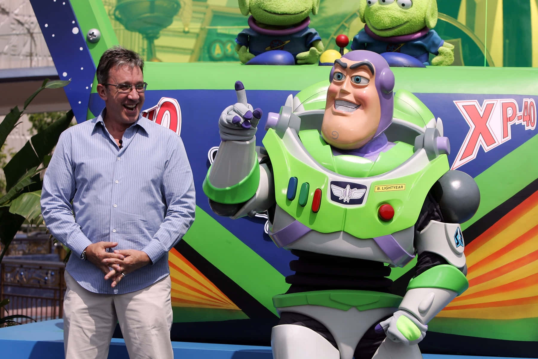 Buzz Lightyear 桌布 壁紙 — 一名男子在色彩繽紛的主題公園景點中，在一個巨大的巴斯光年雕像旁邊大笑。
