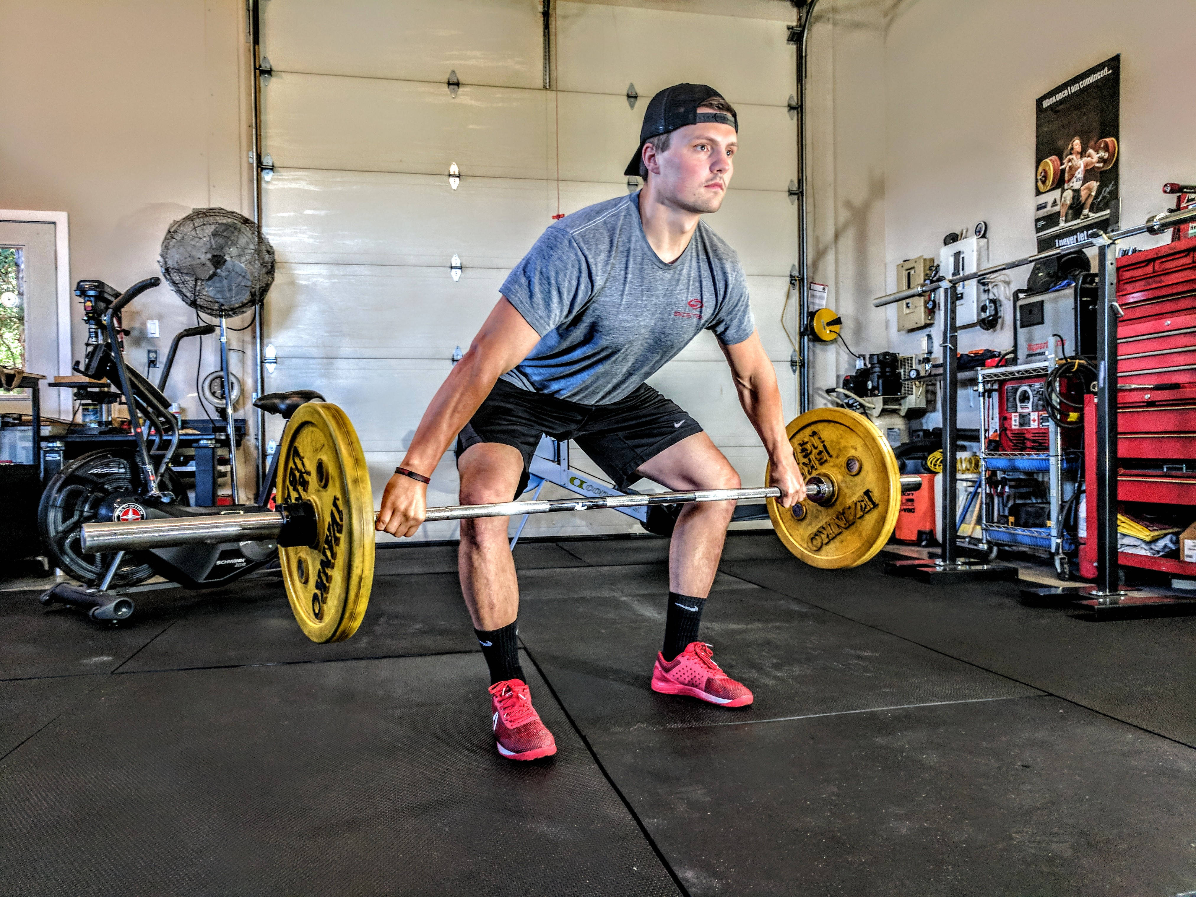 Exercise 桌布 壁紙 — 一名男子在車庫健身房用帶有亮黃色槓片的槓鈴進行硬舉。