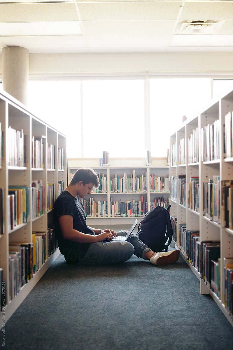 一名男子坐在圖書館地板上的照片 壁紙