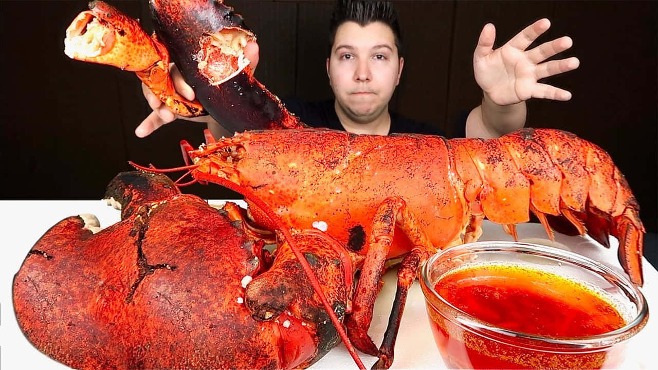 Lobster 桌布 壁紙 — 一名男子展示一隻巨大的熟龍蝦，蝦鉗被打開，旁邊有一碗蘸醬。