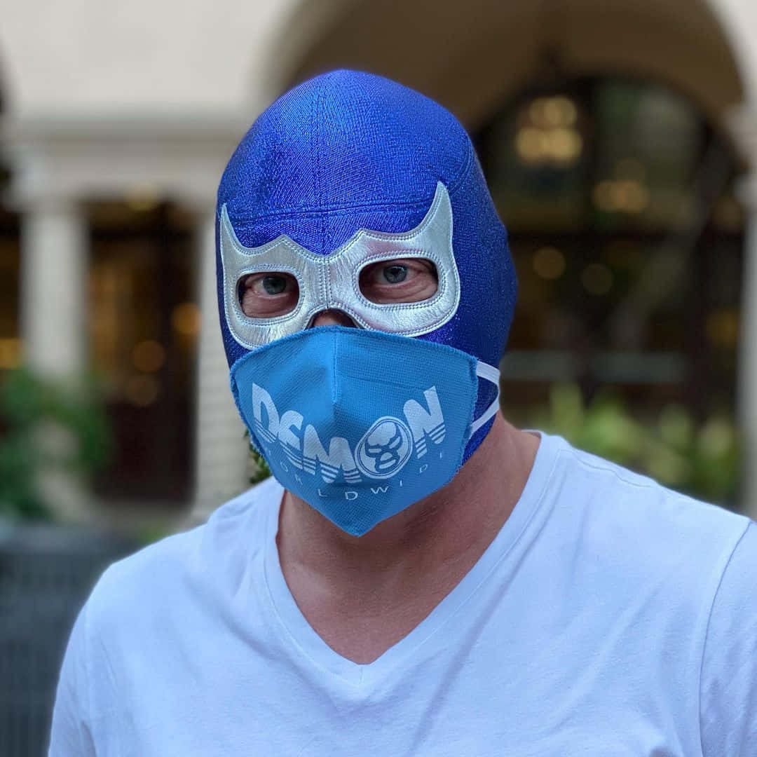 Mexican 桌布 壁紙 — 一名男子戴著帶有銀色裝飾的藍色自由摔角面具和品牌口罩，背景是模糊的建築物。