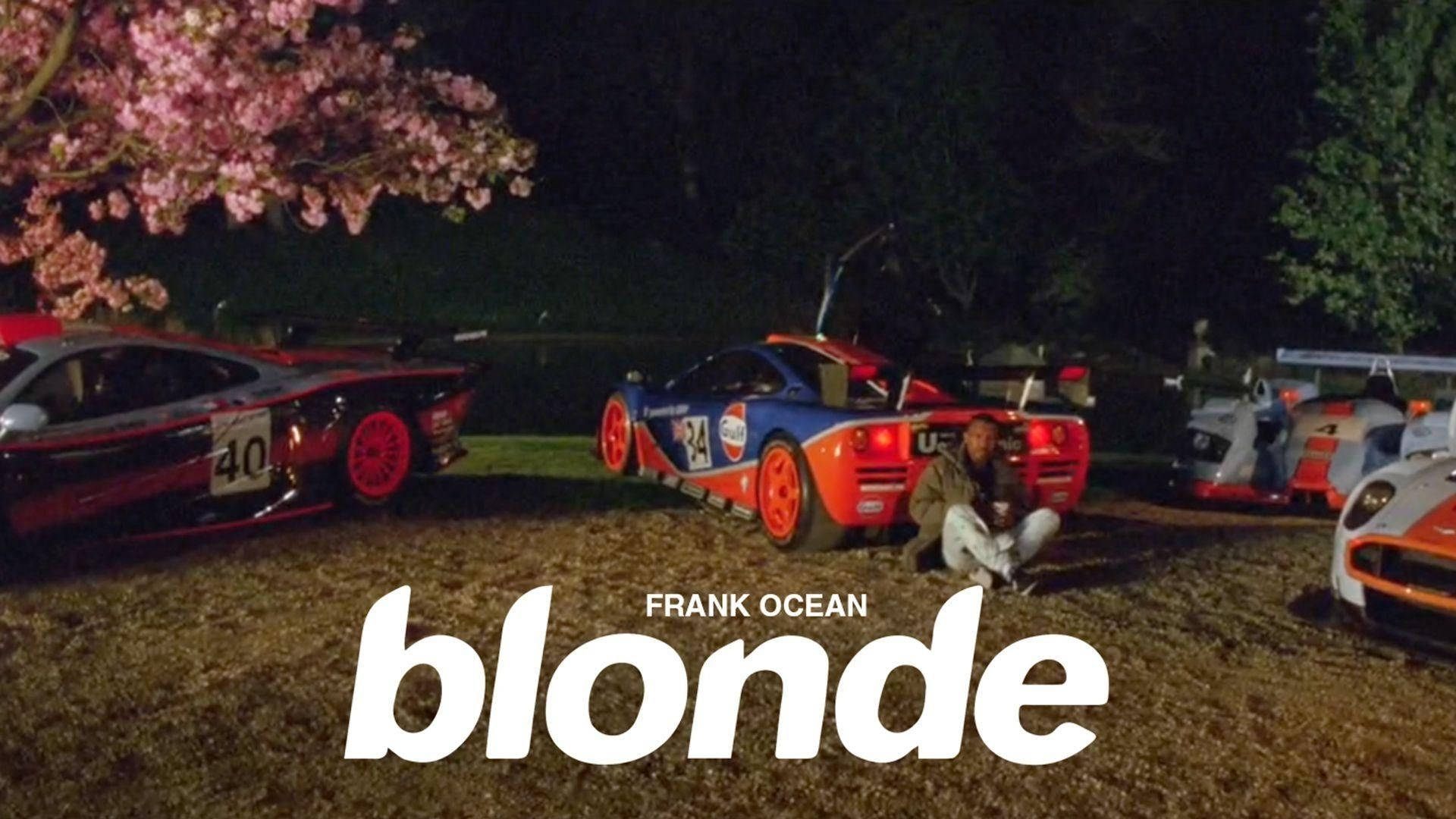 Frank Ocean 桌布 壁紙 — 一名男子晚上坐在草地上，旁邊是充滿活力的賽車，上方是發光的粉紅櫻花。