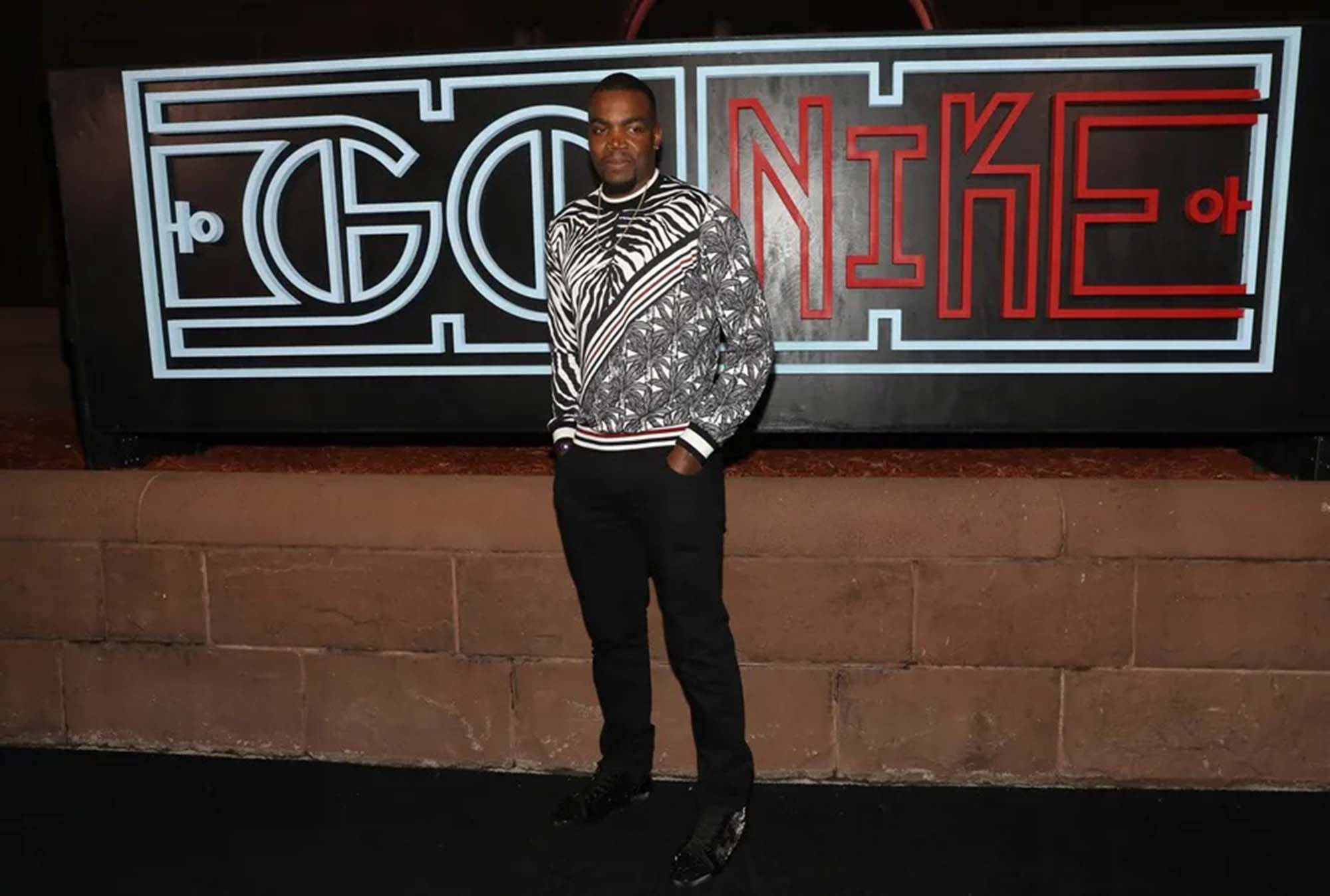 paul millsap 桌布 壁紙 — 一名男子穿著大膽的黑白圖案毛衣，在夜間自信地站在發光的「GO NIK」標誌前。