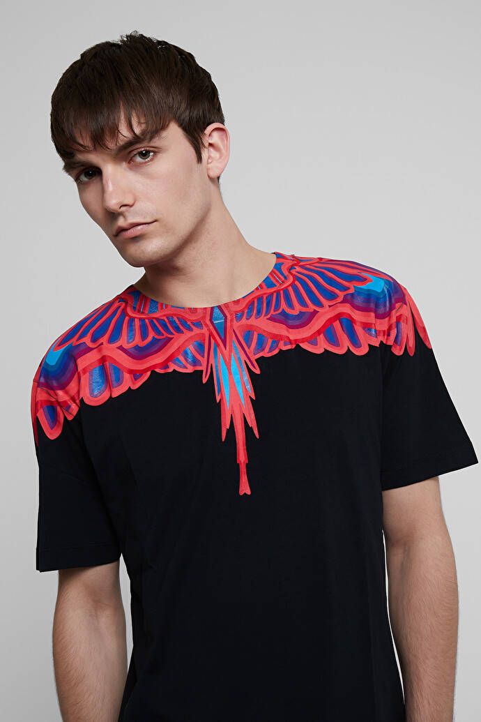 Fashion Model 桌布 壁紙 — 一名男子穿著黑色T恤，肩上有大膽的紅色和藍色翼狀圖案，背景為純灰色。