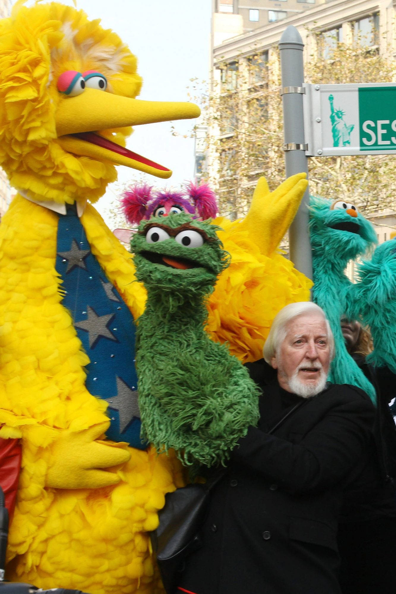 Big Bird 桌布 壁紙 — 一名男子站在大型芝麻街布偶旁邊，包括大鳥和奧斯卡，在一個城市街道場景中。