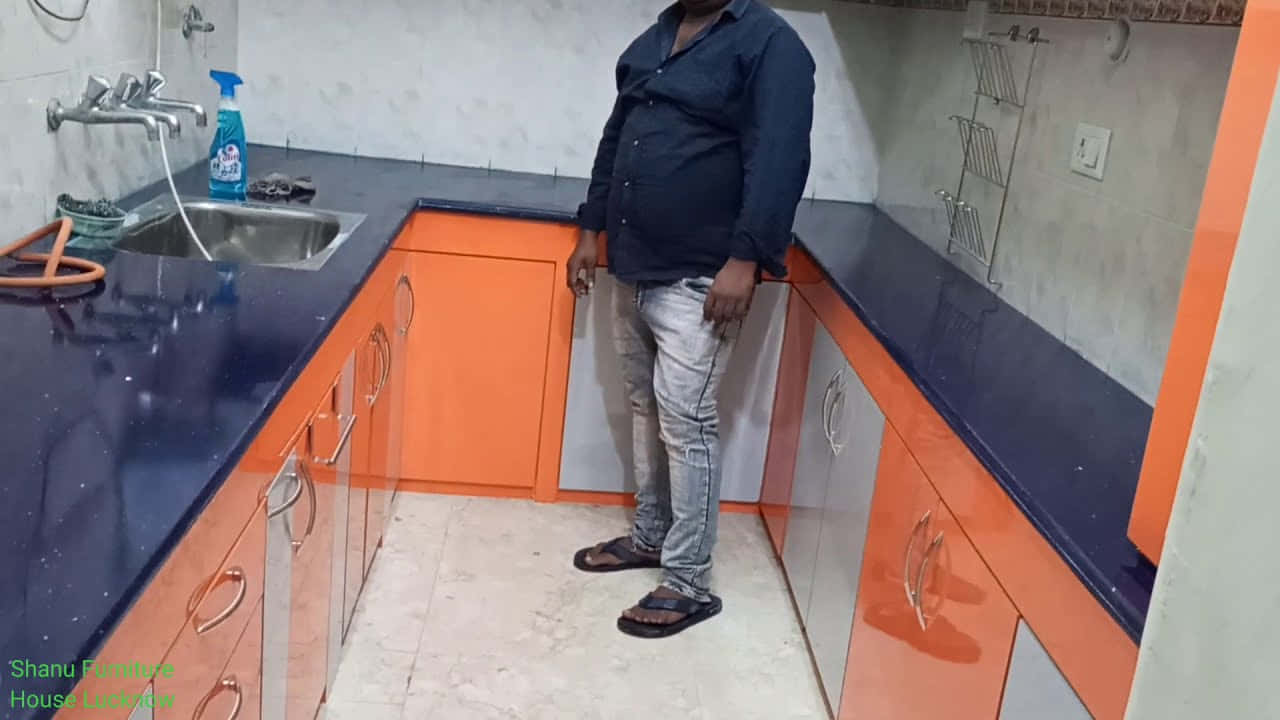 Man 桌布 壁紙 — 一名男子站在現代廚房裡，廚房有鮮豔的橙色櫥櫃和深藍色檯面，光線明亮。