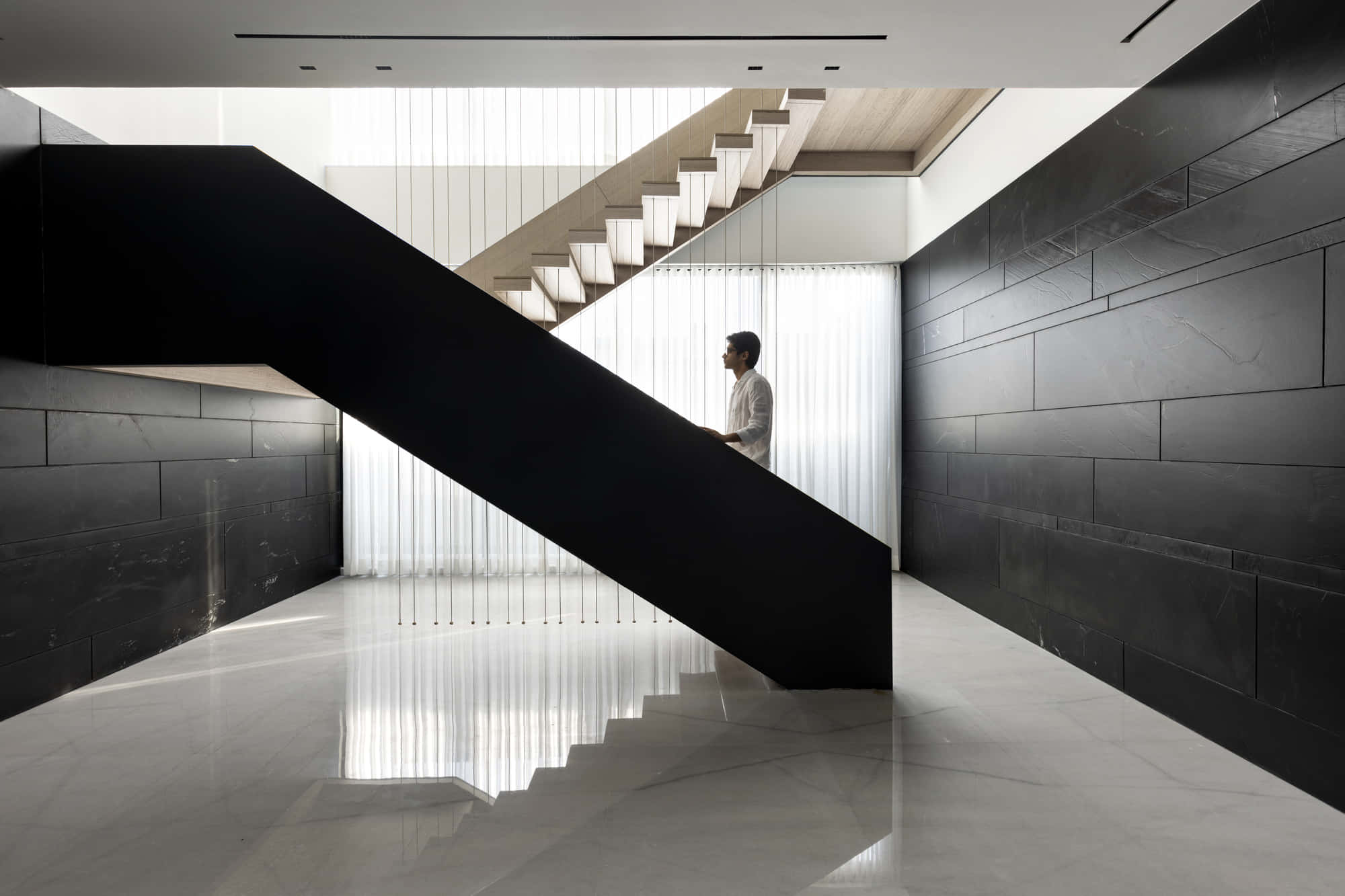 Minimalist Architecture 桌布 壁紙 — 一名男子站在現代風格的懸浮樓梯上，黑色牆壁和白色大理石地板在明亮日光下。