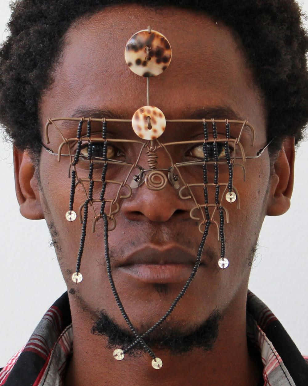 Afrofuturism 桌布 壁紙 — 一名男子臉上飾有複雜的鐵絲和珠子裝飾，包括玳瑁圓片和垂墜珠子，背景為純色。