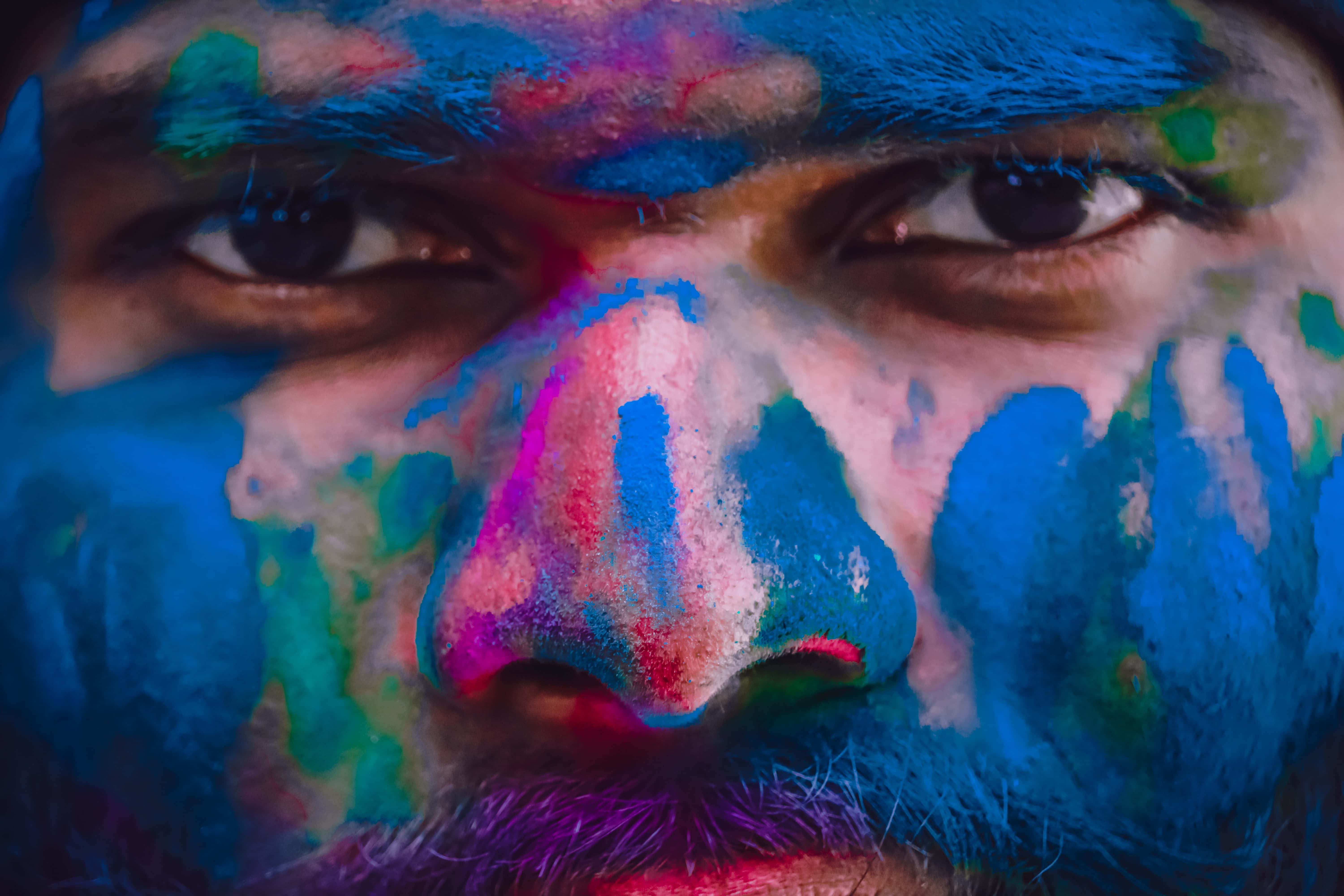 Holi 桌布 壁紙 — 一名男子臉部特寫，在色彩繽紛的節日期間，臉上覆蓋著鮮豔的藍色、粉紅色和綠色粉末。