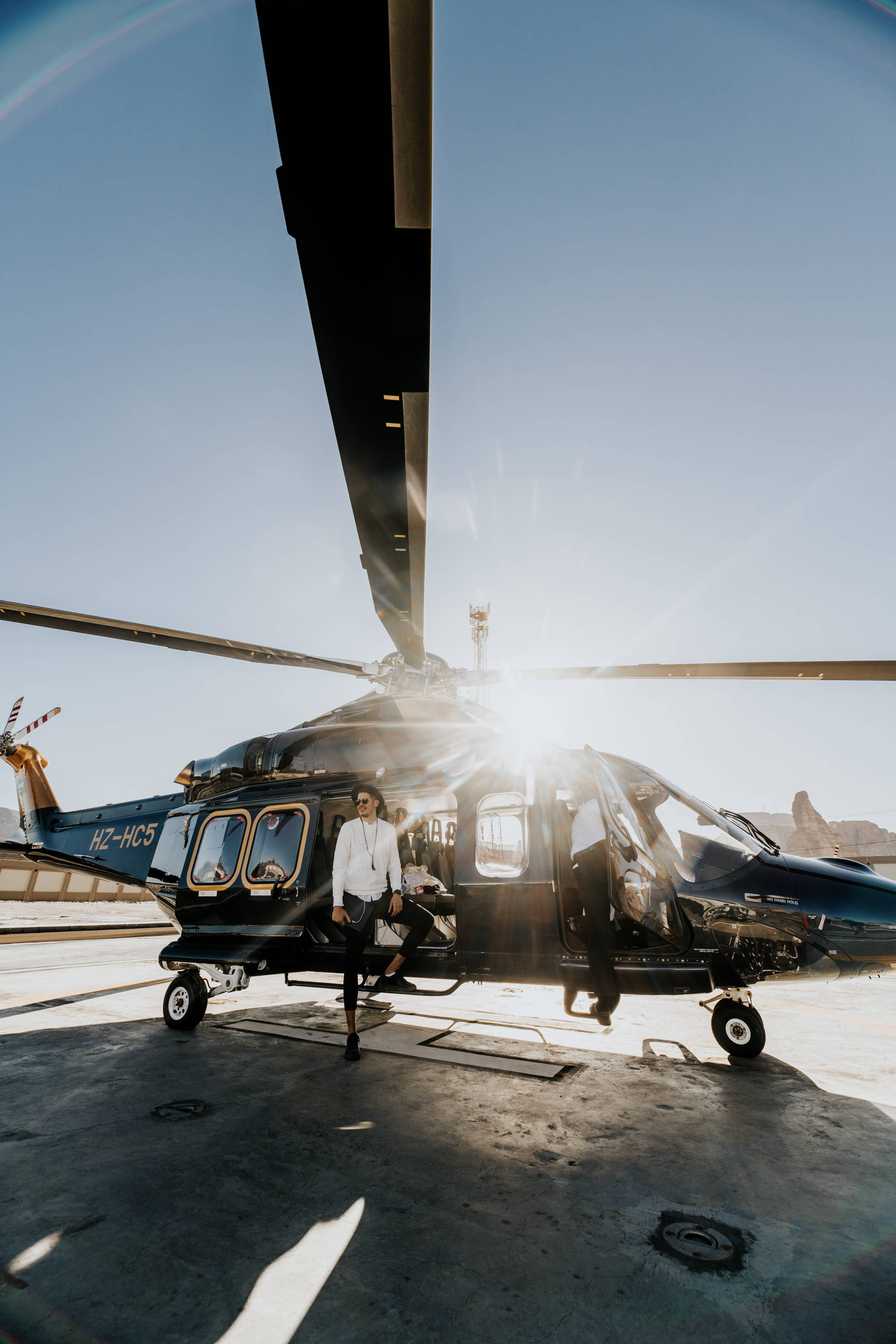 Helicopter 桌布 壁紙 — 一名男子自信地站在一架時尚的黑色直升機旁邊，背景是明亮的太陽耀斑和停機坪。