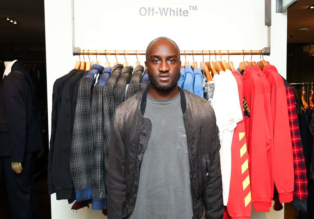 Off White 桌布 壁紙 — 一名男子自信地站在展示Off-White品牌服裝的衣架前，身處零售店內。