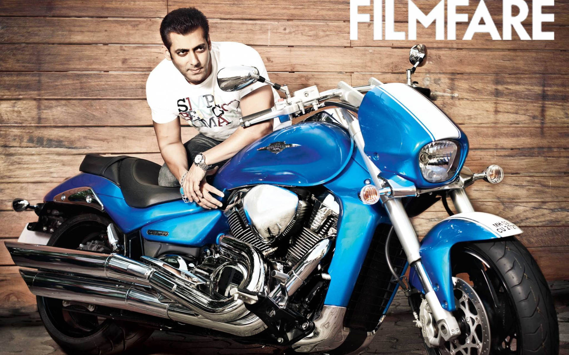 Salman Khan 桌布 壁紙 — 一名男子自信地靠在一輛閃亮的藍色摩托車上，背景是質樸的木牆，上方有「FILMFARE」字樣。