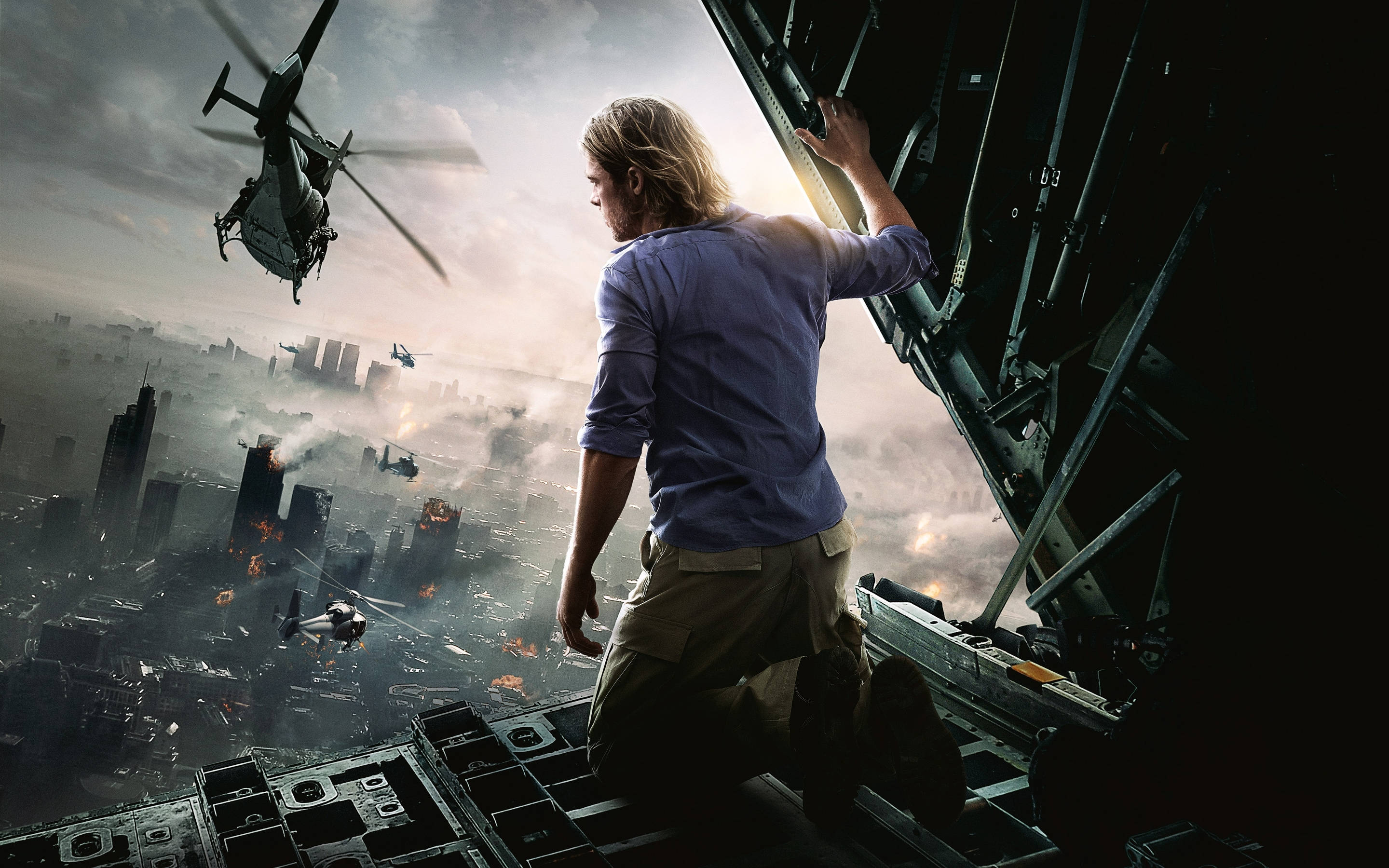 world war z 4K 桌布 壁紙 — 一名男子跪在戰機邊緣，俯瞰著一座燃燒的城市，直升機在煙霧瀰漫的天空中飛行。