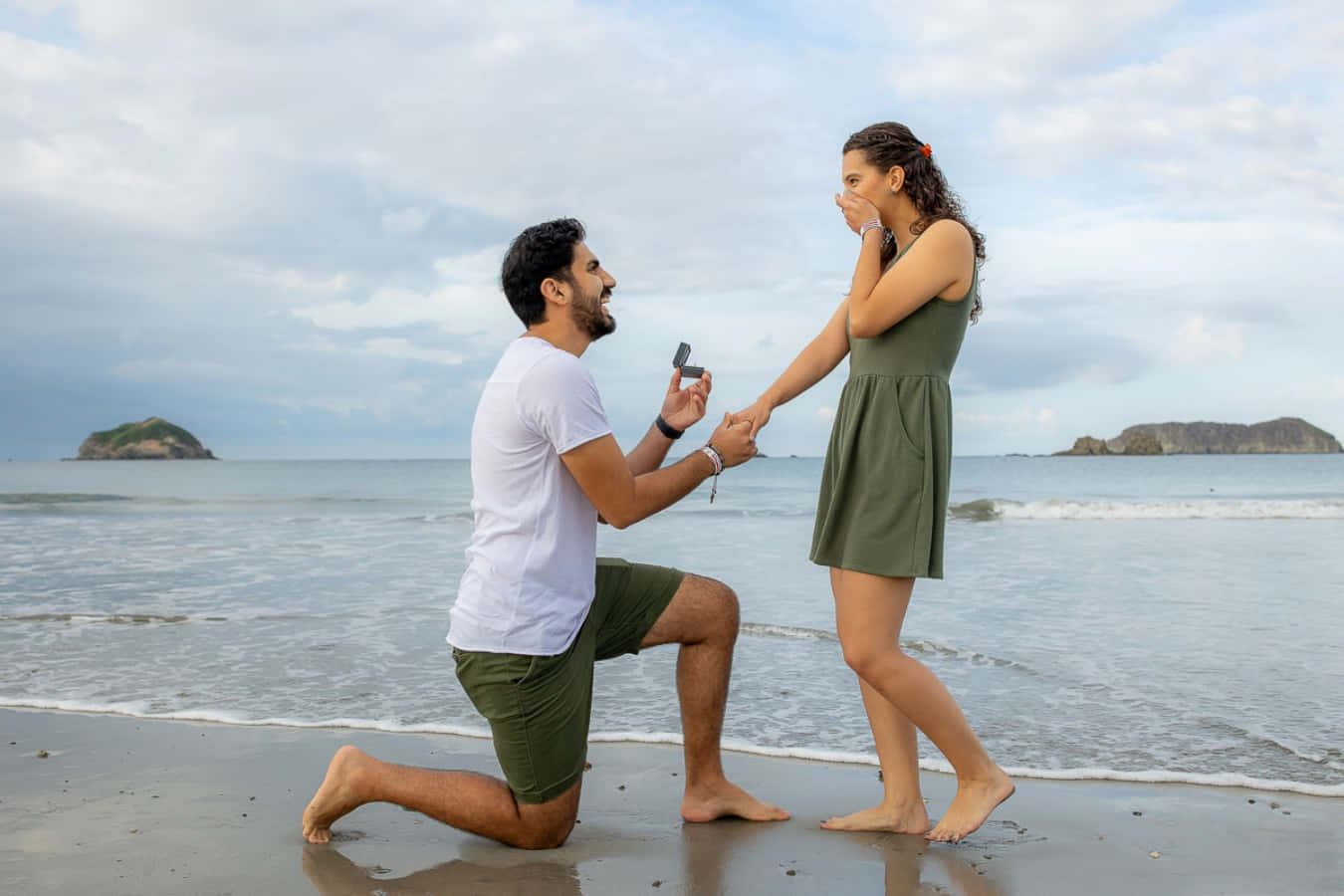 Proposal 桌布 壁紙 — 一名男子跪在沙灘上，手持戒指盒，而一名女子在他旁邊表現出驚訝和喜悅。