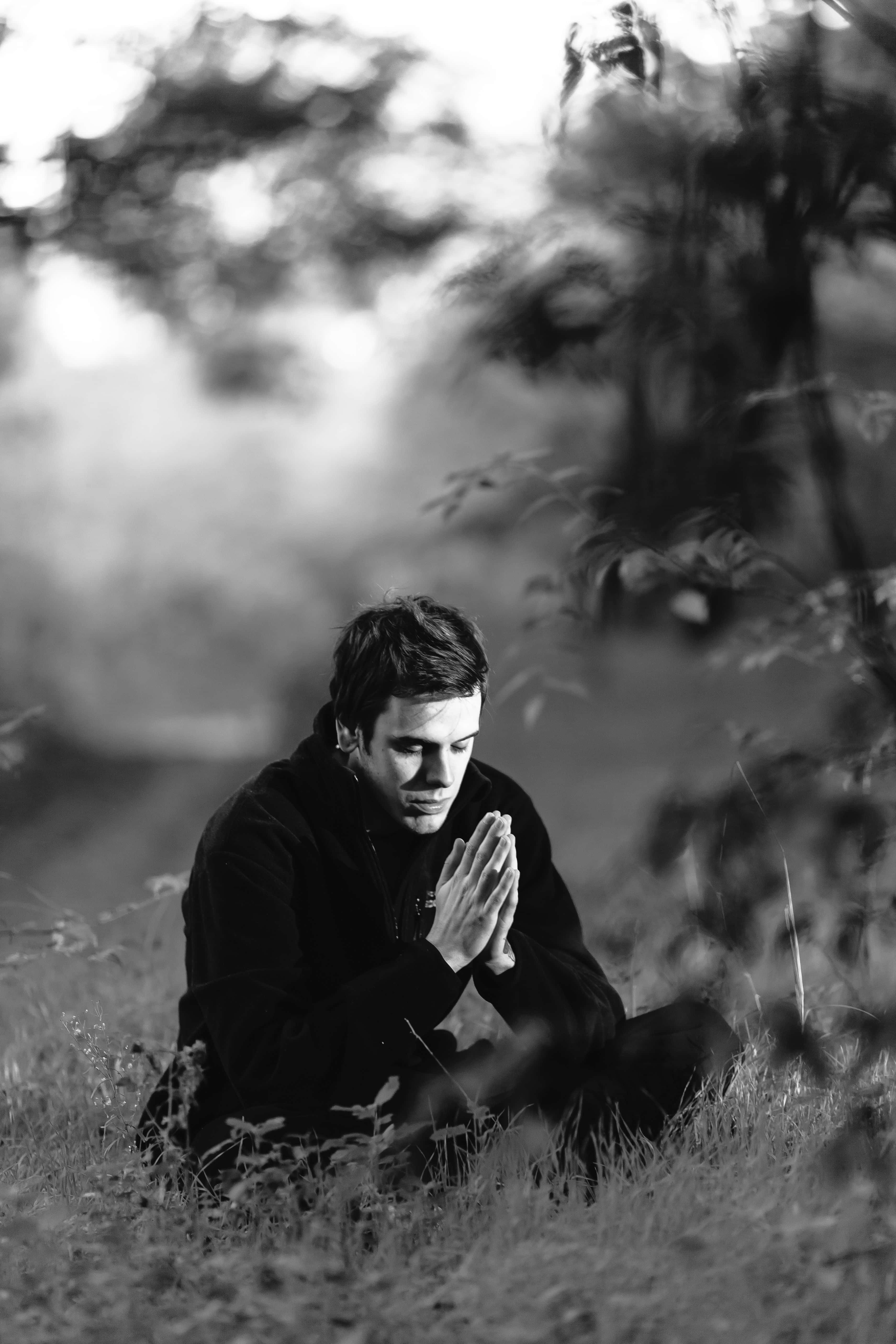 Praying 桌布 壁紙 — 一名男子跪在草地上，雙手合十祈禱，柔和自然光下，背景是模糊的森林。