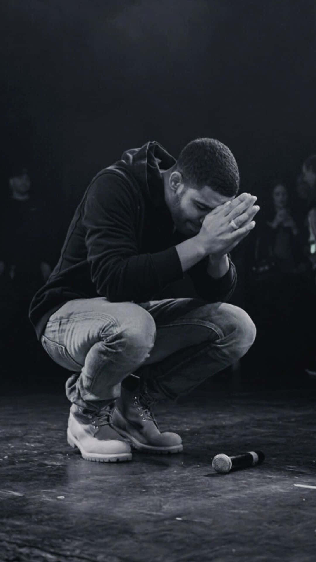 Aesthetic Drake 桌布 壁紙 — 一名男子跪在黑暗的舞台上，雙手掩面，旁邊有一個被遺棄的麥克風。
