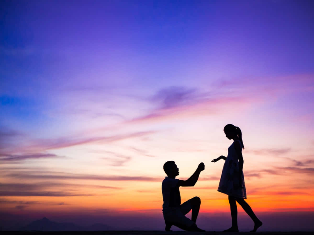 Proposal 桌布 壁紙 — 一名男子跪地向一名女子求婚，背景是充滿活力的紫橙色日落天空和遠處的山脈。