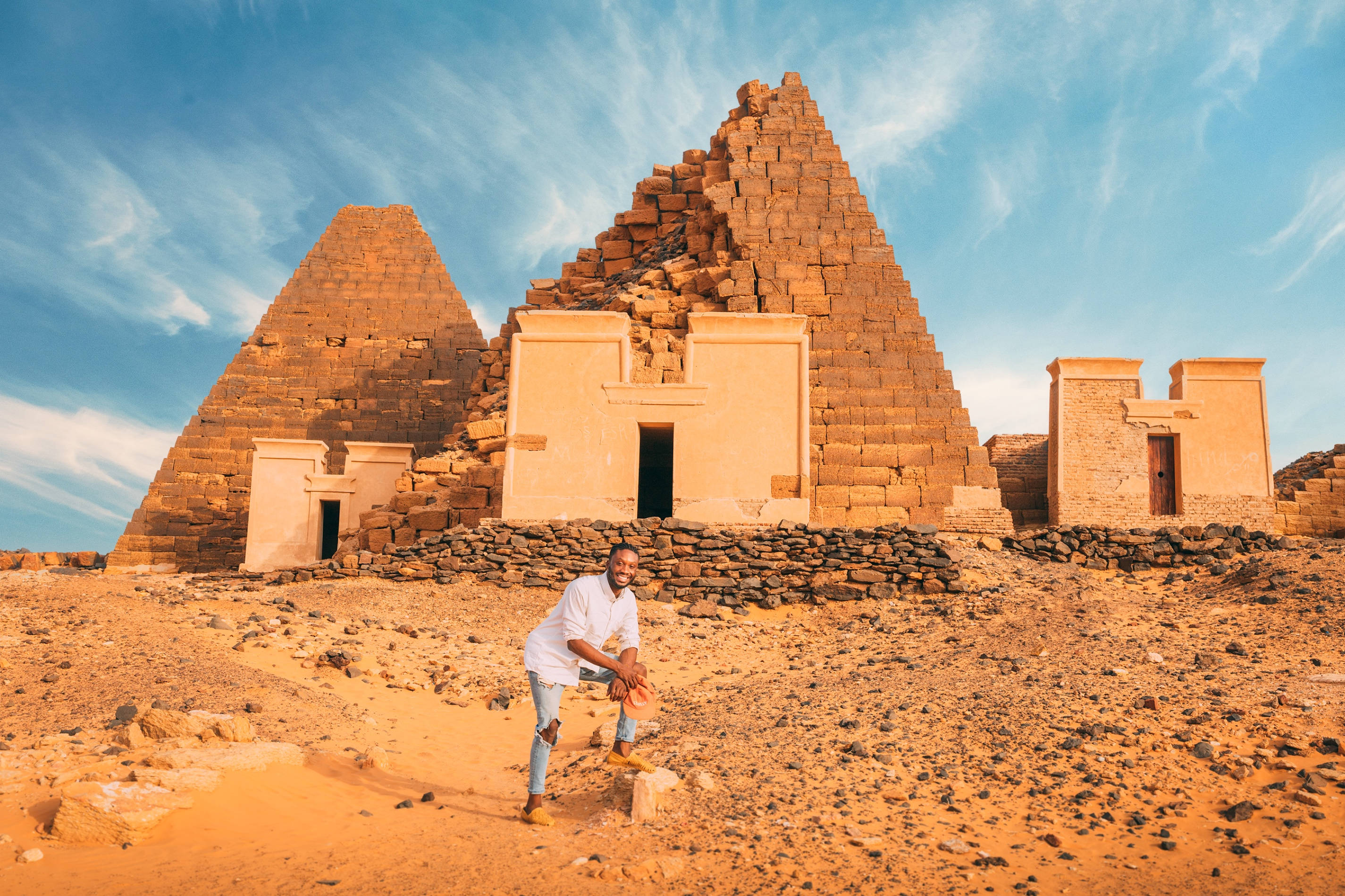 Sudan 桌布 壁紙 — 一名男子蹲在古老石金字塔前，天空湛藍，薄雲飄逸。