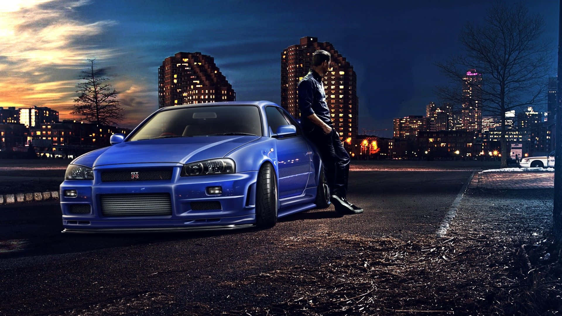 Nissan Skyline 桌布 壁紙 — 一名男子靠在一輛停在潮濕城市街道上的鮮藍色跑車旁，背景是燈火通明的摩天大樓，時間是黃昏。