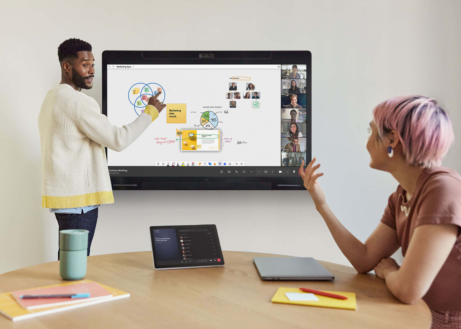 Microsoft Teams 桌布 壁紙 — 一名男性和一名女性在現代辦公室中使用大型互動螢幕，顯示市場行銷圖表和遠端視訊通話參與者，進行協作。